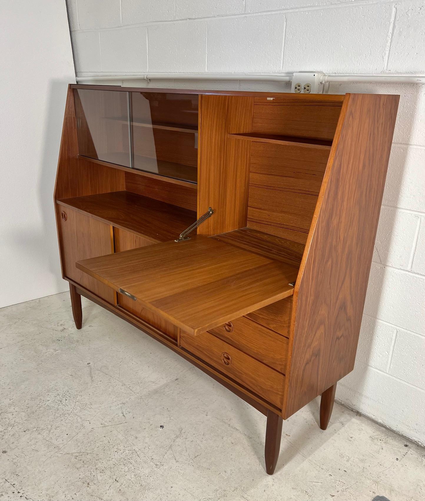 Mid century modern versatile teak highboard. Featuring a drop down cabinet that can be used as a small secretary desk or a bar.
Three drawers and a cabinet with sliding doors and fixed shelf at the bottom.

Condition: Very good condition. Minor