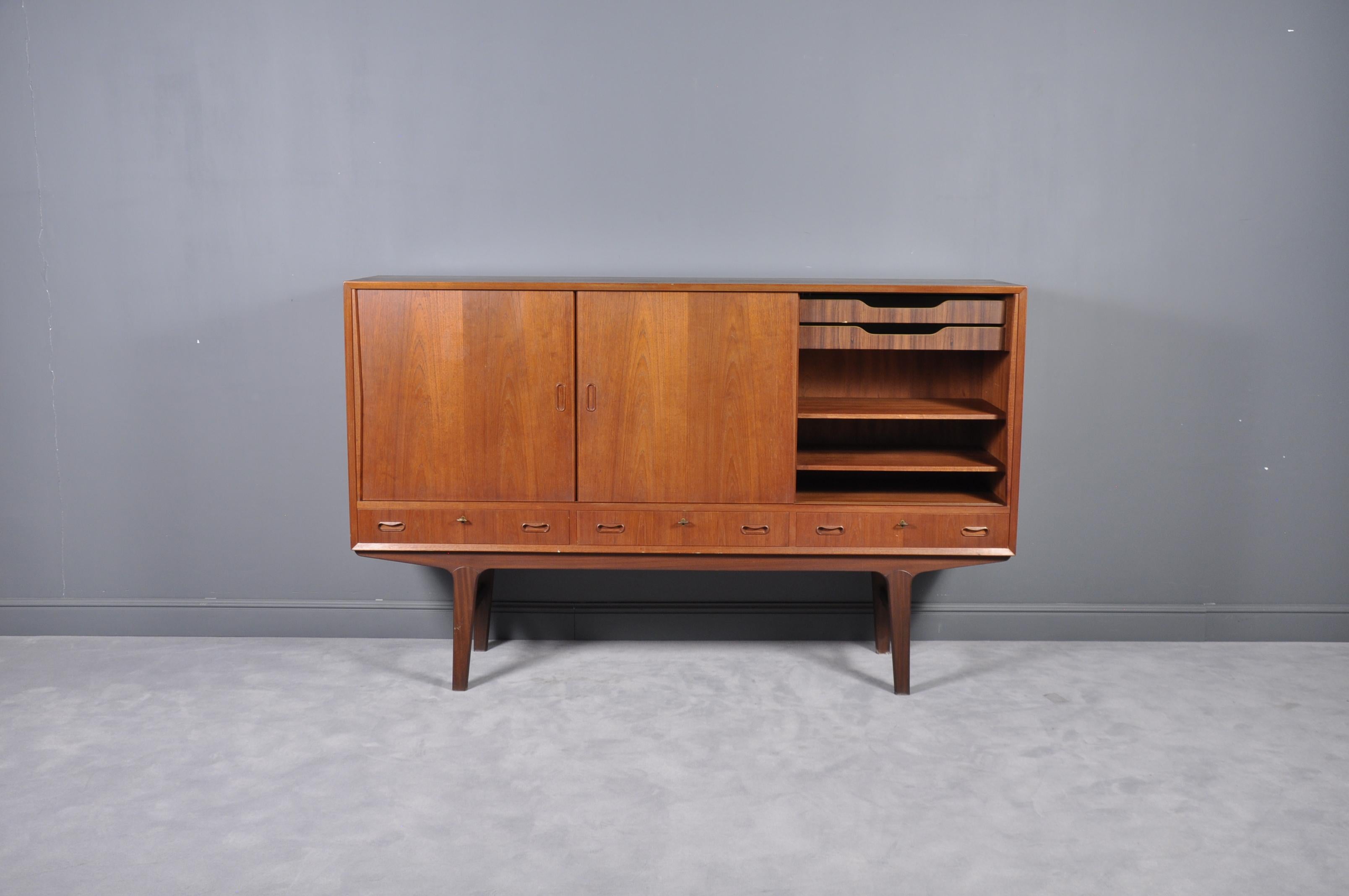 This Scandinavian highboard or credenza was manufactured in Denmark in the 1960s. It features four sliding doors and three separate drawers. The doors, shelves, and legs are made of solid teak, and the frame is teak veneered to ensure a higher