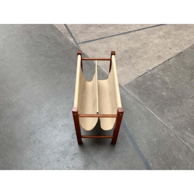 Elegant mid-century teak magazine rack.

The finely crafted frame made of solid teak wood elements is striking. The actual shelf consists of a coarse canvas fabric clamped into the frame. The central bar is made of brass.

The condition is very good