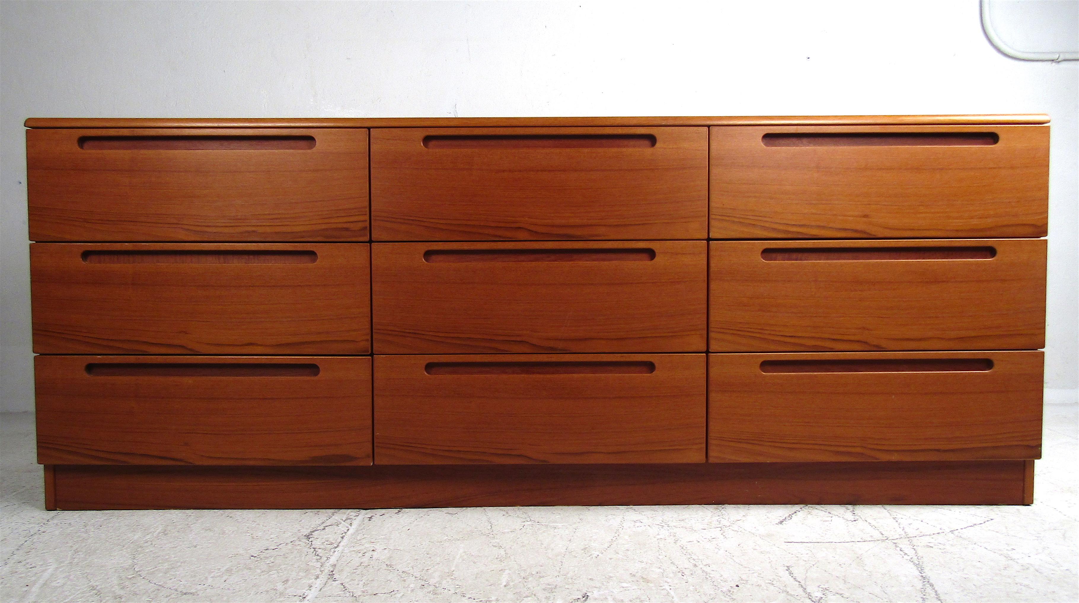 This stunning vintage modern dresser provides ample storage within its nine hefty drawers. A unique straight-line design with recessed oblong drawer pulls and a rich teak finish. This gorgeous midcentury case piece makes the perfect addition to any