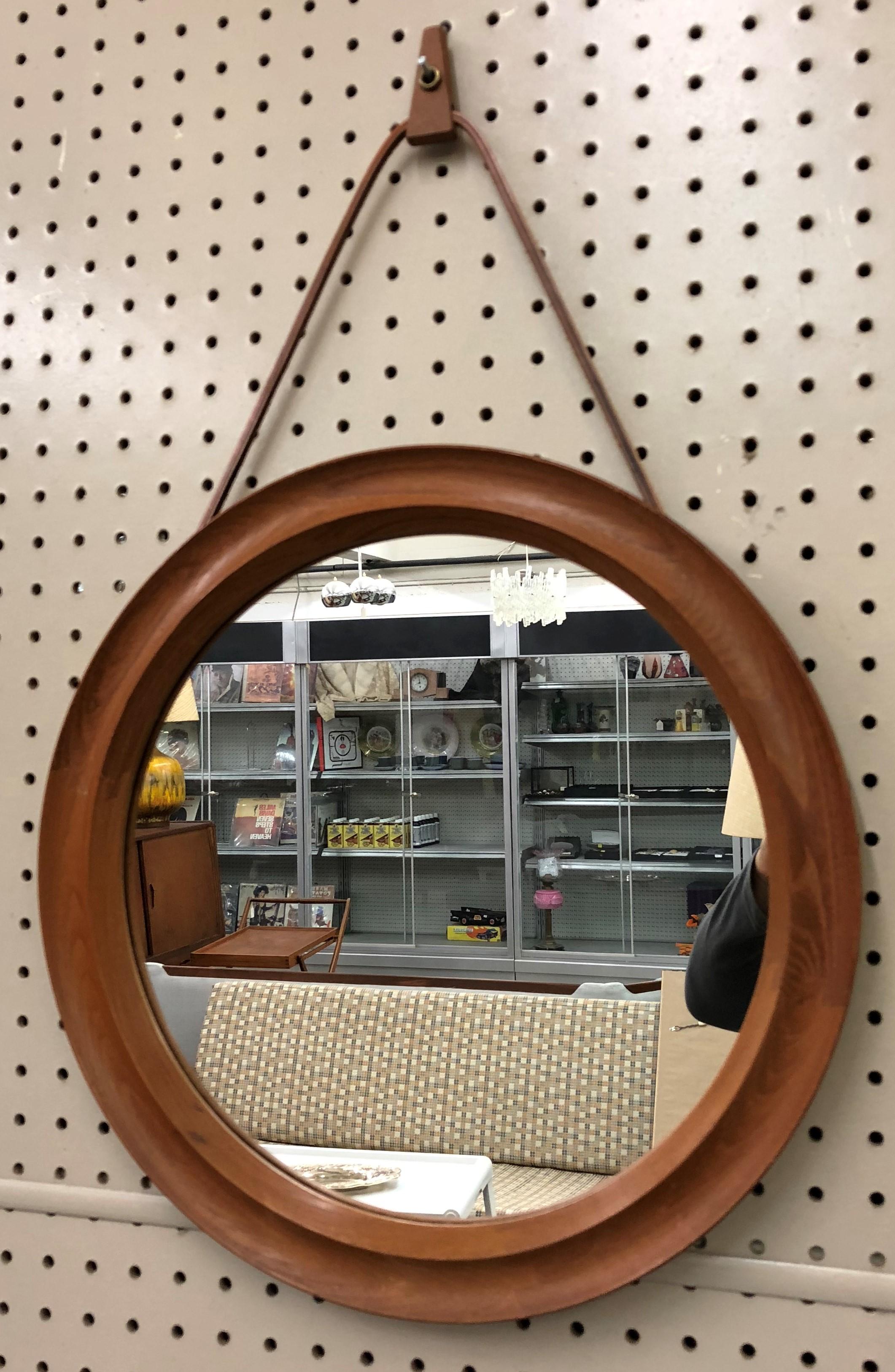 Teak Danish oval mirror made by Pedersen and Hansen (Viby J. made in Denmark)  Hangs from a brown leather strap to create a minimalist appearance and a teak wood nail holder, measuring 15.75 inches round. 

Mid-Century Modern / Scandinavian Modern