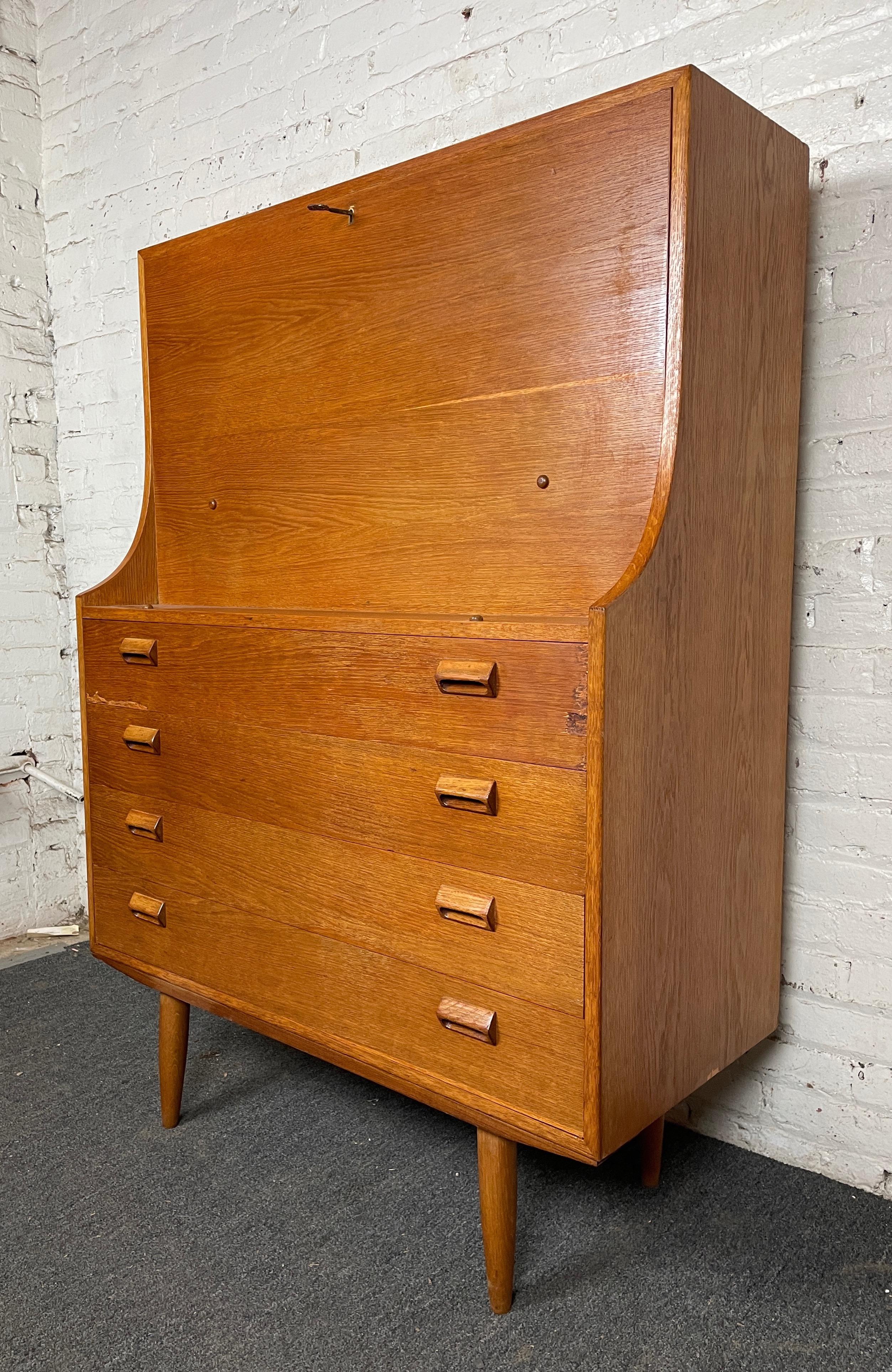 Beautiful vintage modern teak secretary desk from Denmark. The desk features four spacious drawers with sculpted wood handles. Pull on the key to fold down the desk revealing the beautiful workspace, complete with two dovetailed drawers and multiple
