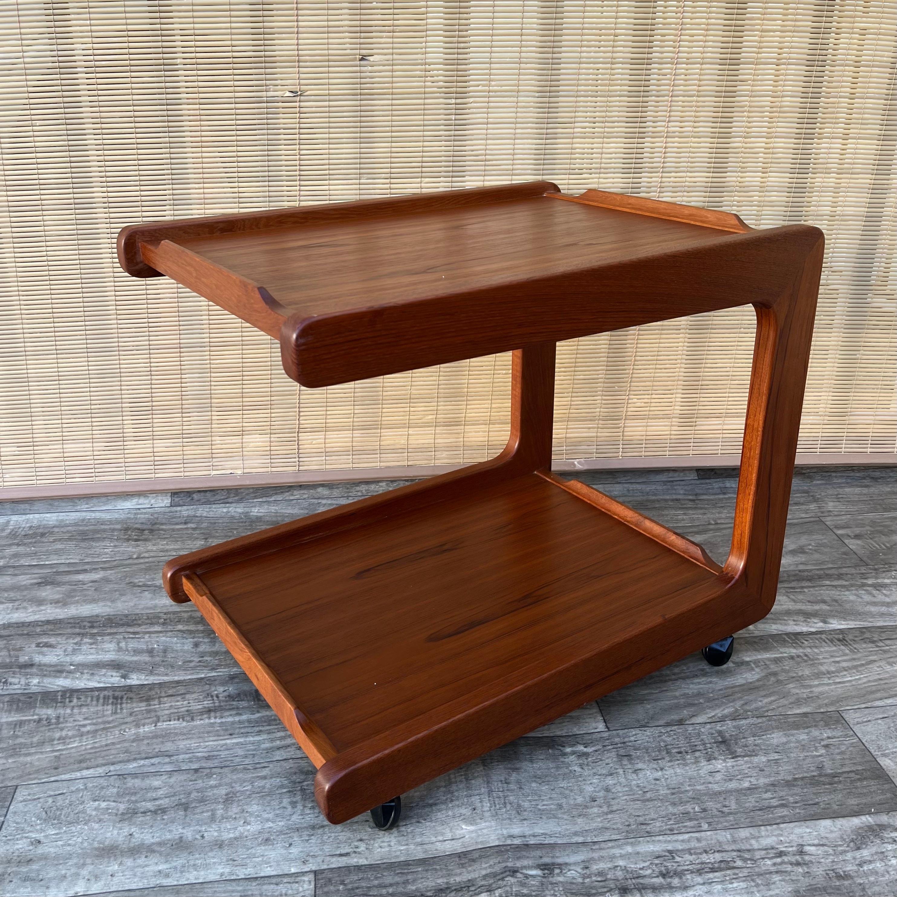 Vintage Mid Century Modern Danish Teak Serving Cart, Circa 1960s
Features a sleek Mid Century Scandinavian C-shaped Design with a cantilever top tier, casters for easy mobility, and a beautiful teak wood grain. 
In excellent near mint original