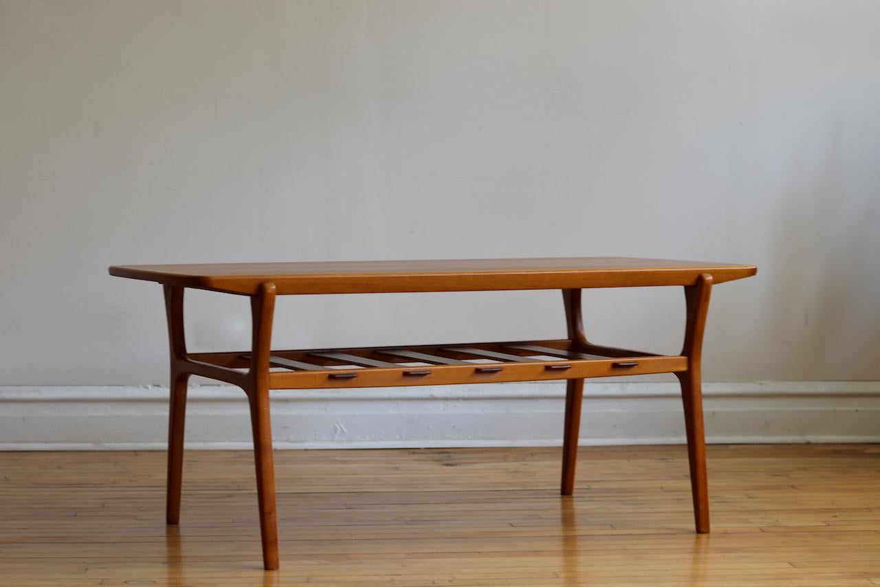 Danish Mid-Century Modern teakwood two-tier coffee table.
Just imported from Denmark!
Gorgeous splayed legs.
Wide slat wood shelving.
Top has a border around it with rounded corners.
Refinished teak.
Excellent vintage condition!
Measures: 50