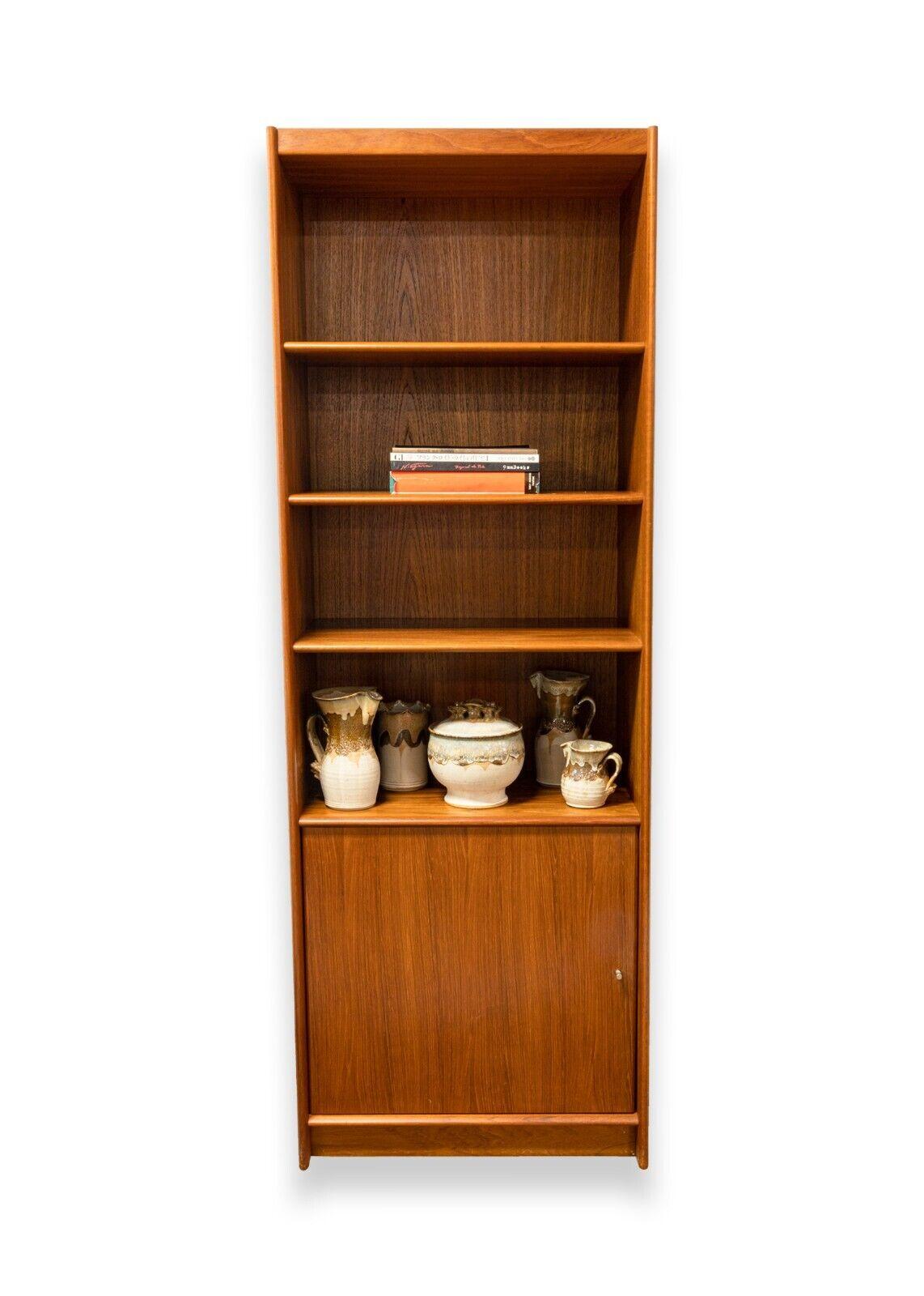 A mid century modern Danish teak wood bookshelf. A wonderful wooden bookcase featuring a lovely teak wood grain, 4 open shelves, and a door revealing two additional shelves. This piece is in very good condition. The back is unfinished, and is marked