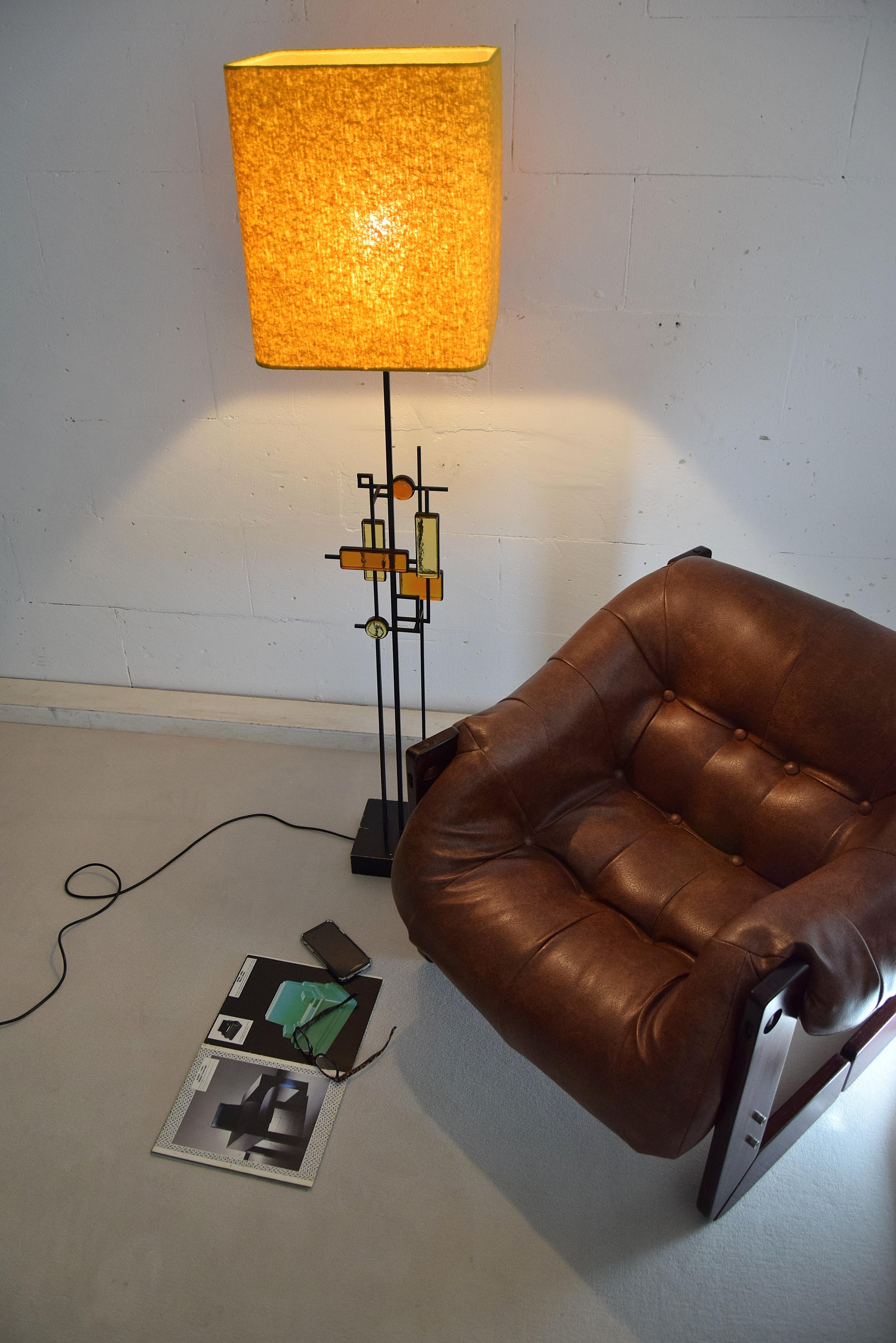 Black wrought iron and glass floor or table lamp. Various pieces of thick amber and yellow glass in geometric shapes framed in black wrought iron and suspended on square thin metal rods above a square wooden base colored black. Designed by Svend