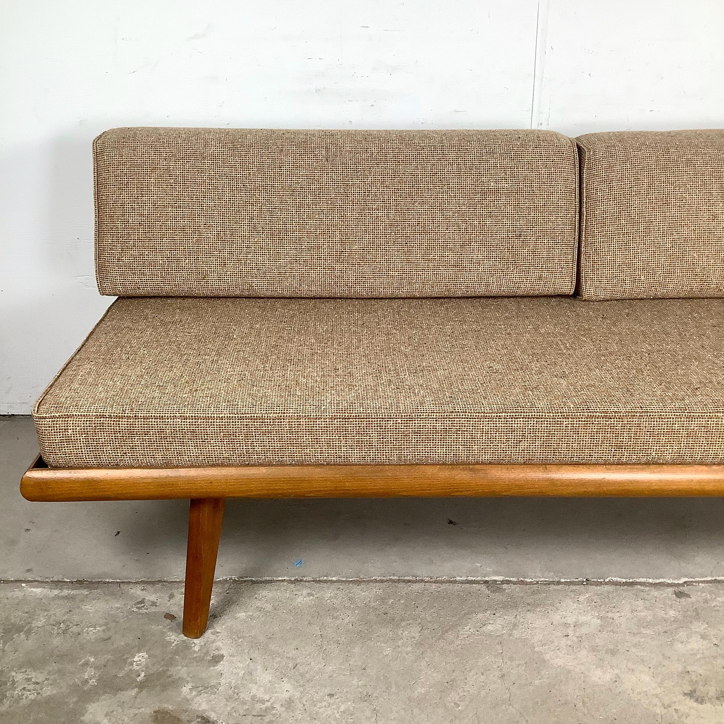 This walnut-framed mid-century modern sofa/daybed invites both stylish seating and spontaneous repose. The combination of minimalist lines, textural upholstery, and warm wood grain provides an ideal foundation for modern living. It’s a nod to the