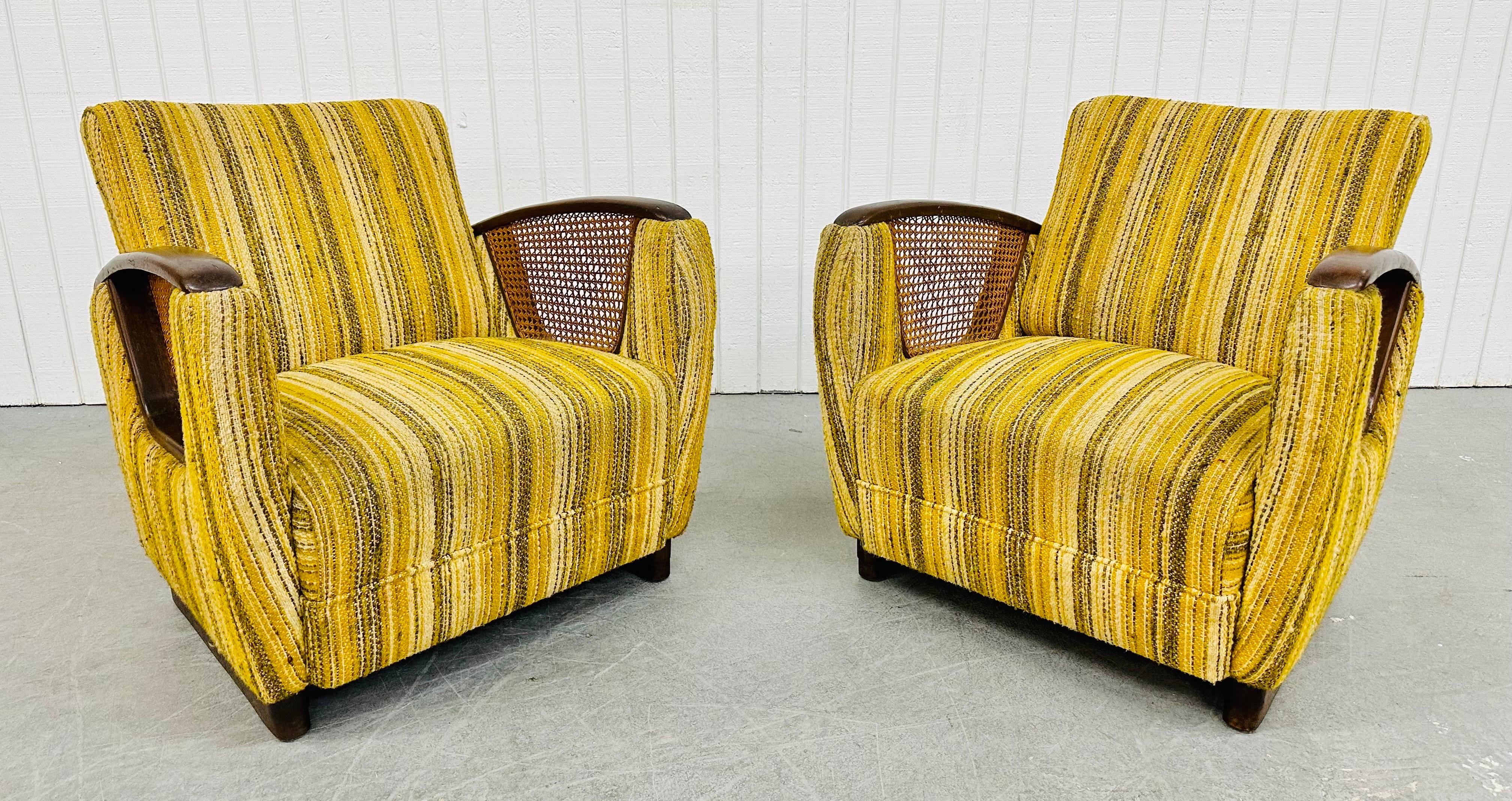 This listing is for a pair of Mid-Century Modern Deco Style Club Chairs. Featuring an Art Deco style design, rounded arms with wooden arm rests, cane sides, original yellow striped upholstery, and modern legs with brass trim. This is an exceptional