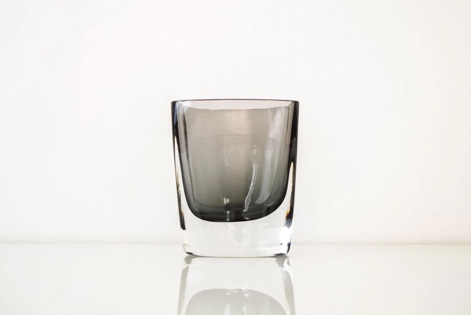 This striking Mid-Century Modern smoked gray glass decorative vase is made from transluscent smoked glass with a thick clear base. It features a beautiful profile with a unique rectangular shape, clean lines and gentle curves.