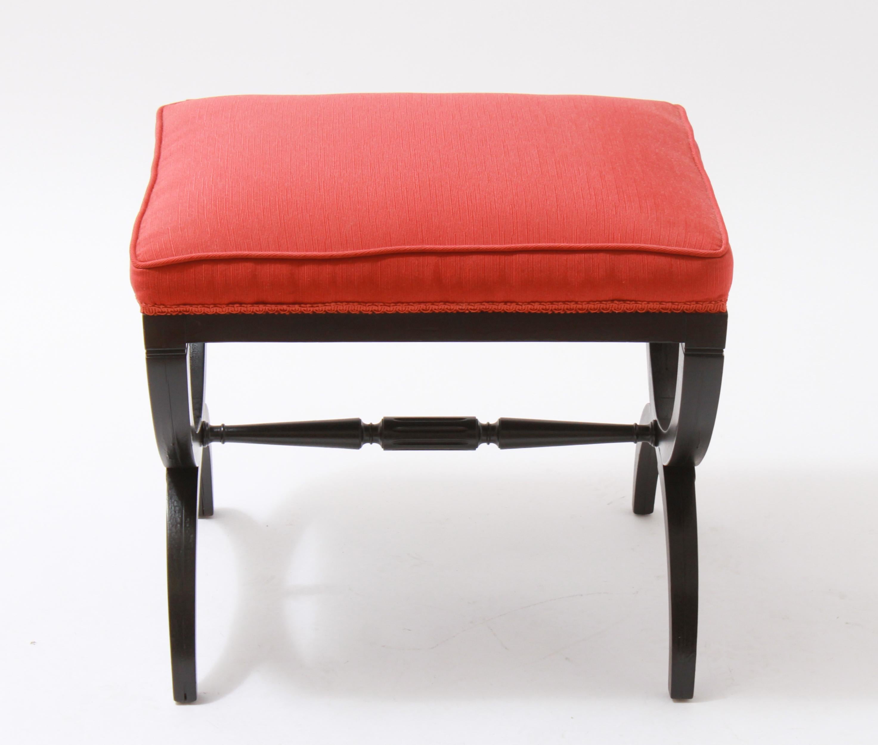 Mid-Century Modern demilune ottoman or stool, attributed to Widdicomb, with a black painted base and a turned fluted stretcher. Recently reupholstered in red upholstery. In good vintage condition with some age-related wear.