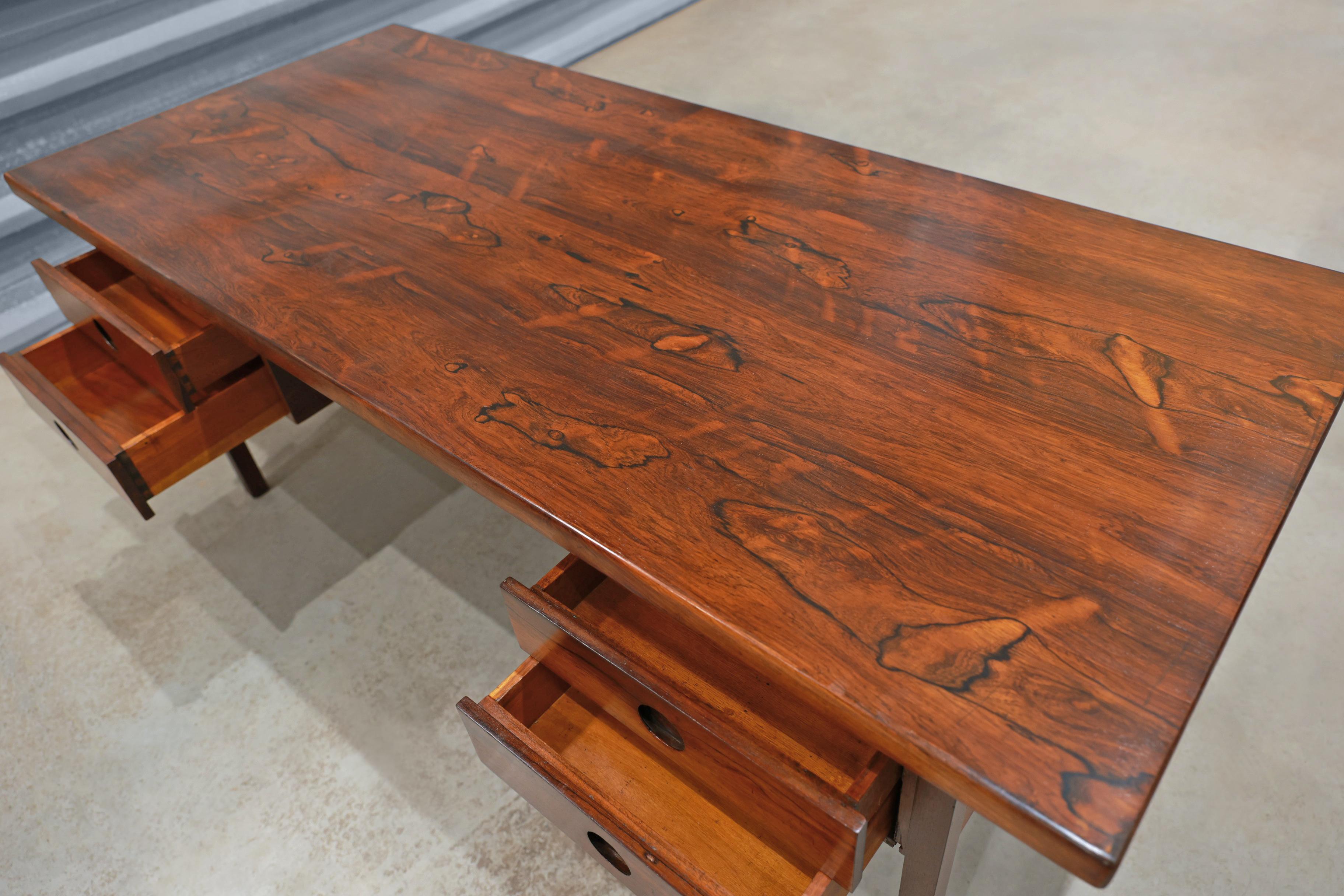 The “Clara” desk is made with Brazilian rosewood, also known as jacaranda, with a rosewood veneer. The hardwood has been expertly refinished, displaying vibrant wood veins. The desk features four drawers (two on each side) with four robust legs.