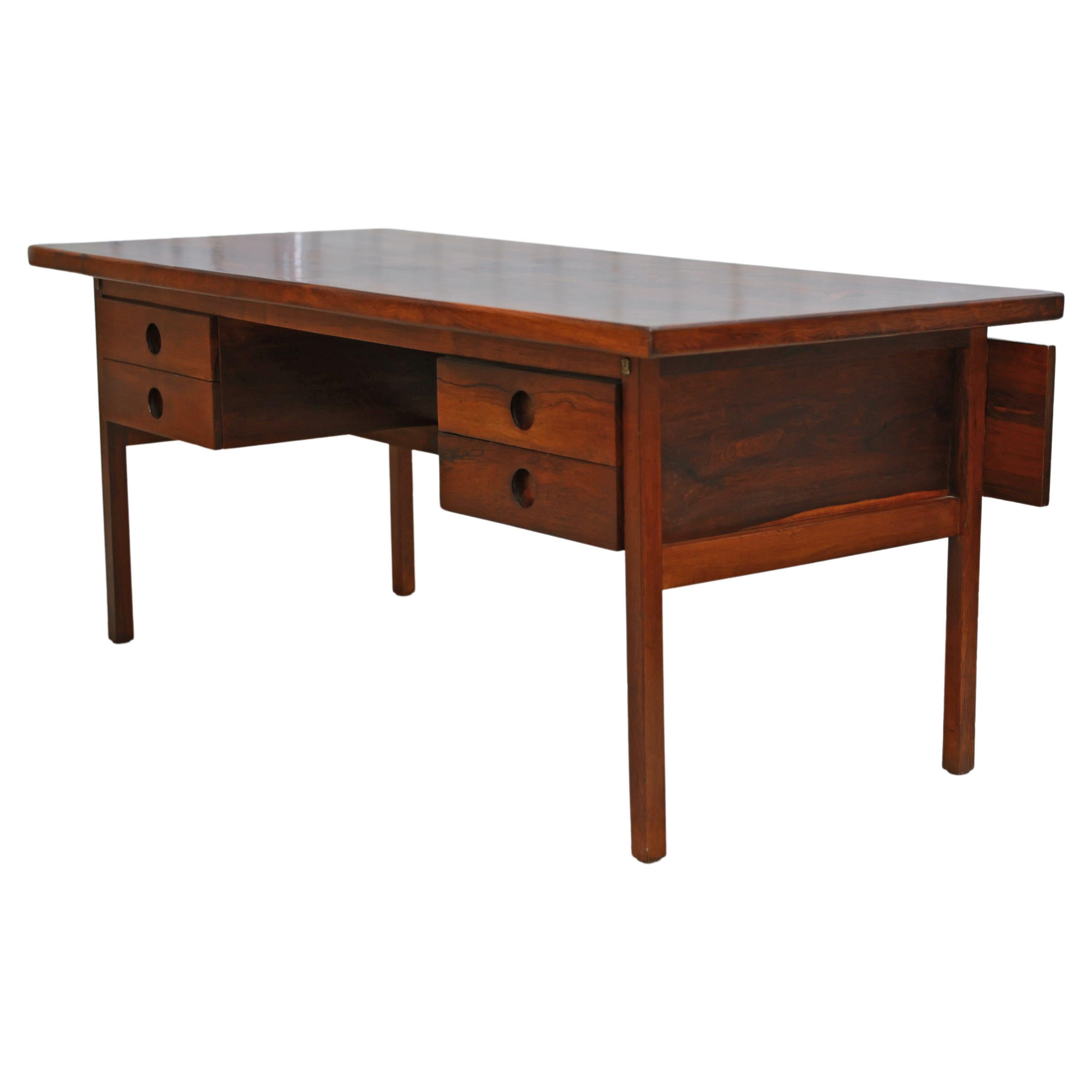 The desk is made with Brazilian rosewood, also known as jacaranda, with a rosewood veneer. The hardwood has been expertly refinished, displaying vibrant wood veins. The desk features four drawers (two on each side) with four robust legs. What makes