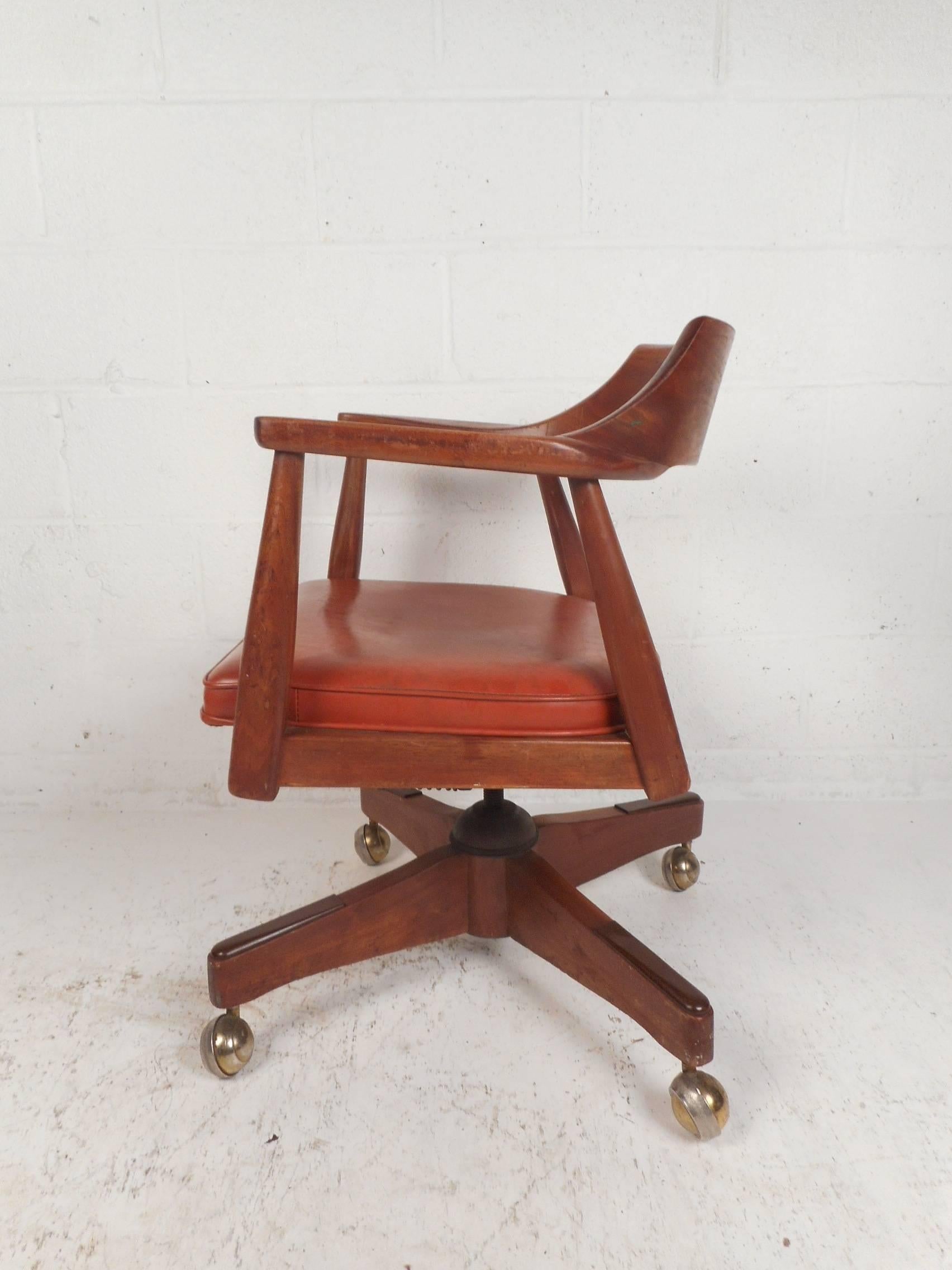 A wonderful vintage modern desk chair on castors with a sculpted backrest. This stylish chair has a solid walnut frame and high arm rests. A thick padded seat covered in red vinyl and a curved backrest ensure plenty of comfort without sacrificing