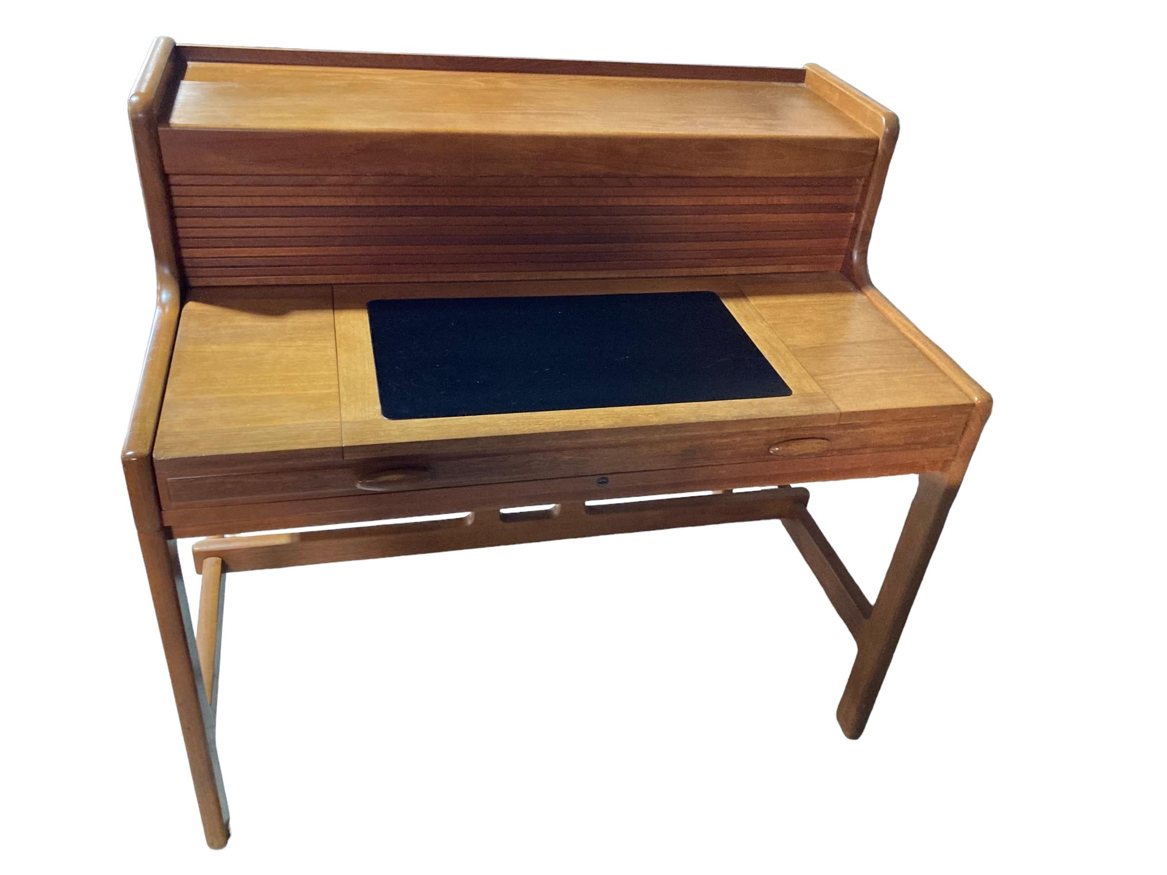 This stunning, Mid-Century Modern desk was designed by John Mortensen and manufactured for Dyrlund. The desk surface pulls forward to raise a tambour door, behind which has a lot of compartments. Small, solid teak drawers on the left side of the