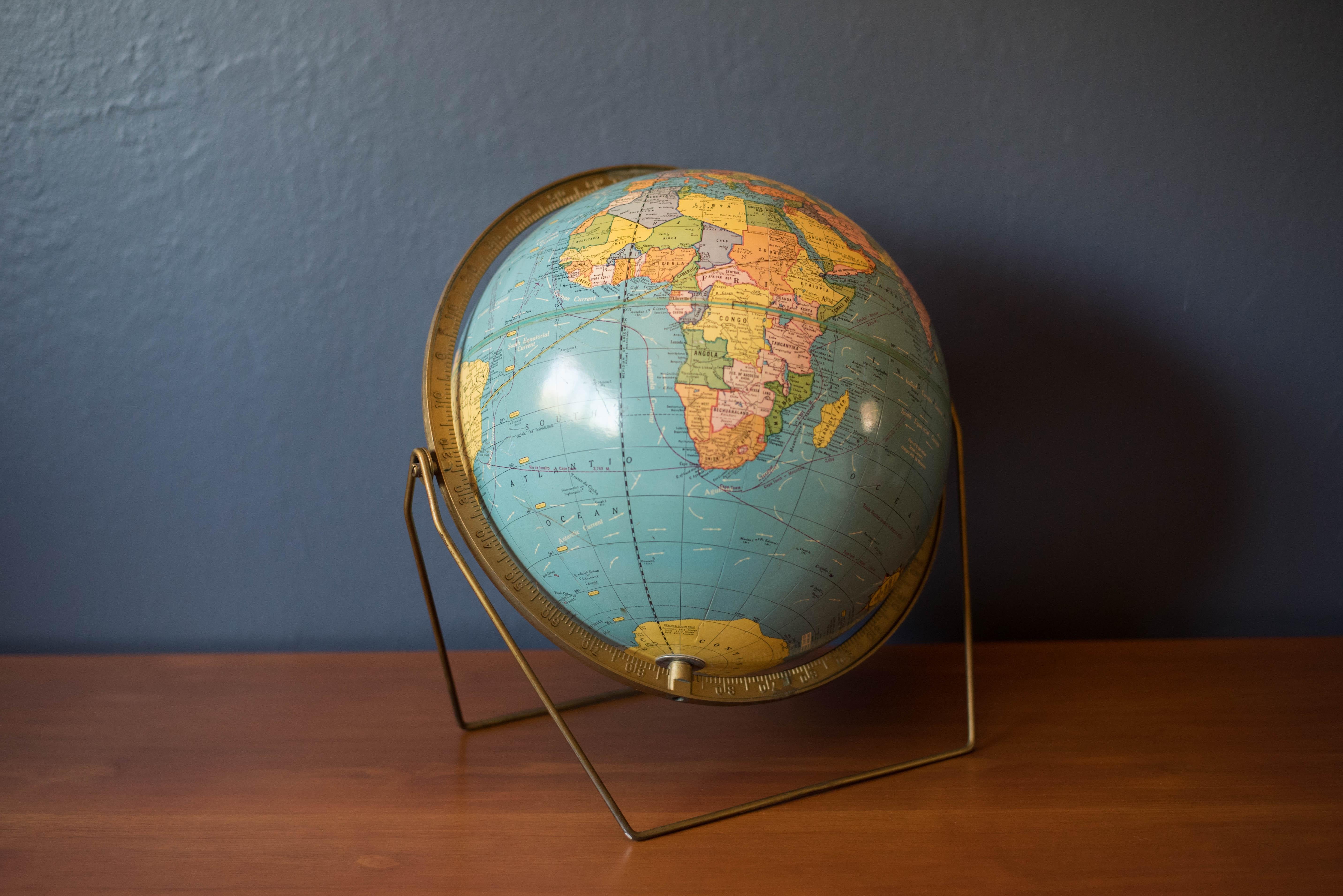 Vintage desk or tabletop globe map with stand in brass by Scholastic. This piece rotates on a full swing meridian and displays plenty of vintage charm. The perfect accessory piece for any home office or library room.