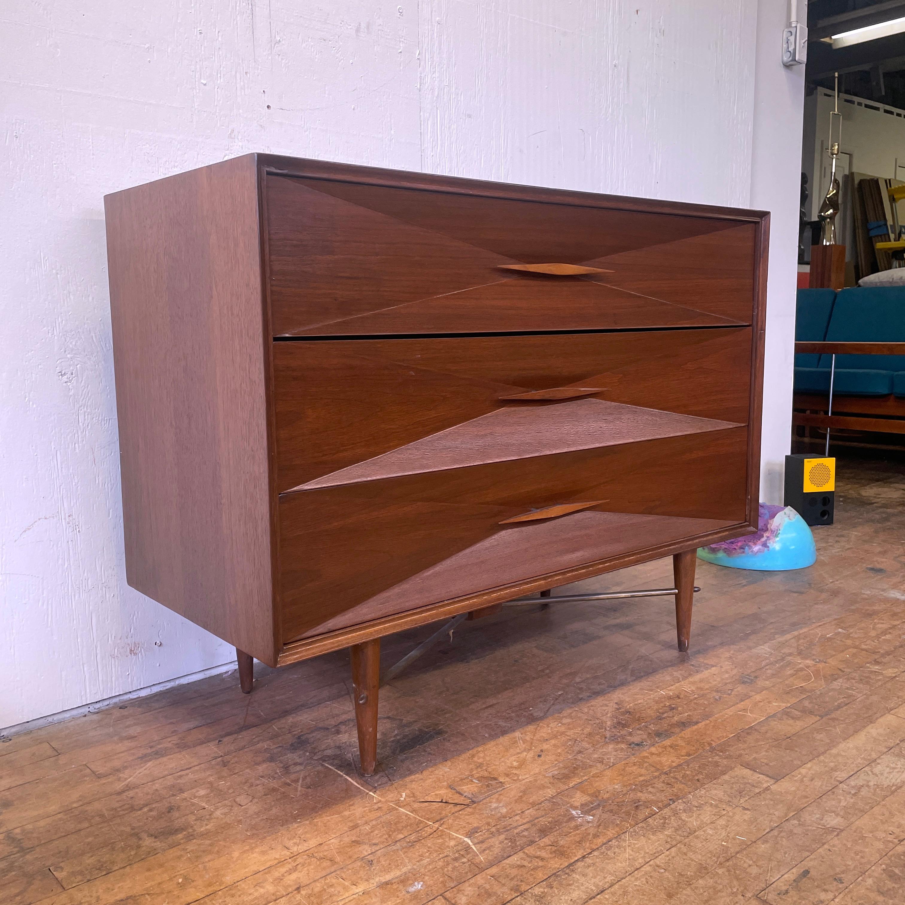 A gorgeous Mid-Century Modern wooden dresser with faceted front and diamond shaped handles; maker unknown. Made of walnut wood with wooden handles. Overall in excellent condition with no scuffs or scratches. One of the metal spacers on one drawer