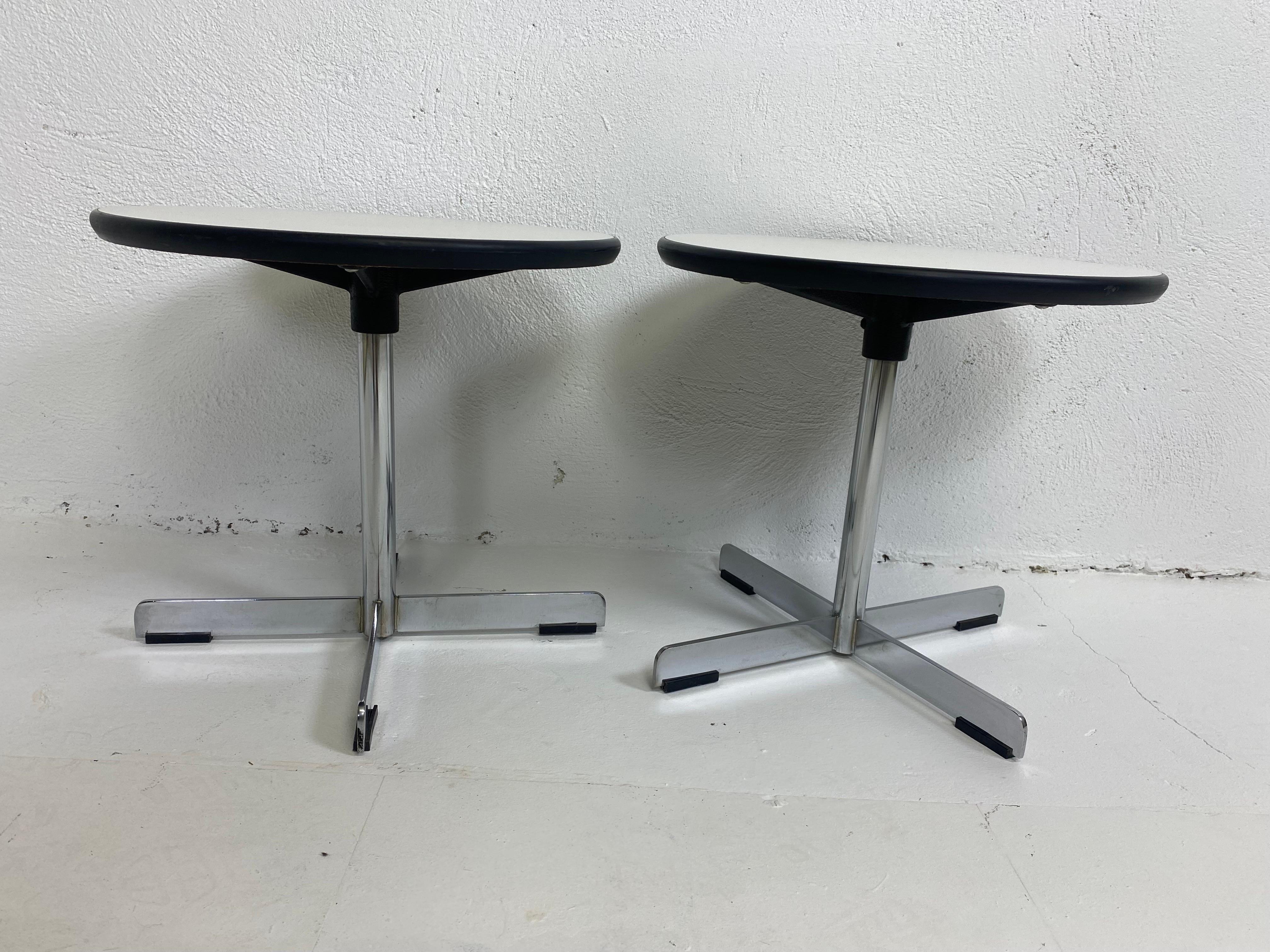 This is a pair of Mid-Century Modern diminutive martini tables/side tables. This pair of tables have a white laminate top with a black edge. The tables have a Chrome pedestal style leg. These tables are in the matter of Florence Knoll circa 1970.
