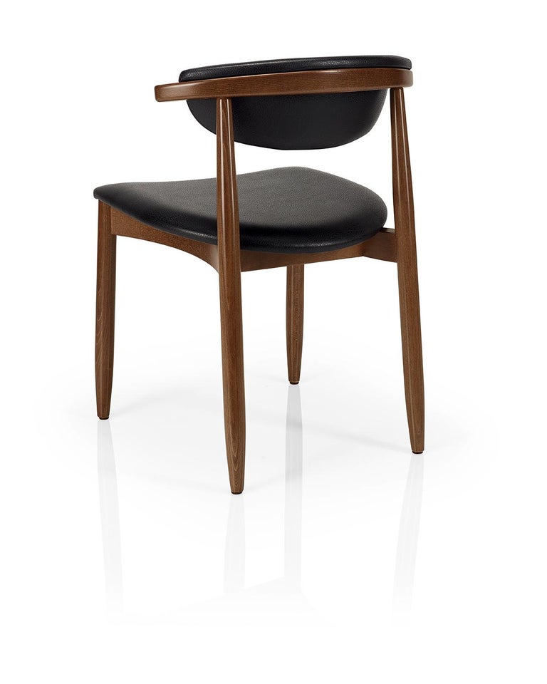 Mid-Century Modern curved back dining chairs upholstered in black faux leather. 
Crafted of solid black wood frame for either casual or formal dining room or kitchen. 
This chair is heavily constructed and suitable for contract use.
100% European