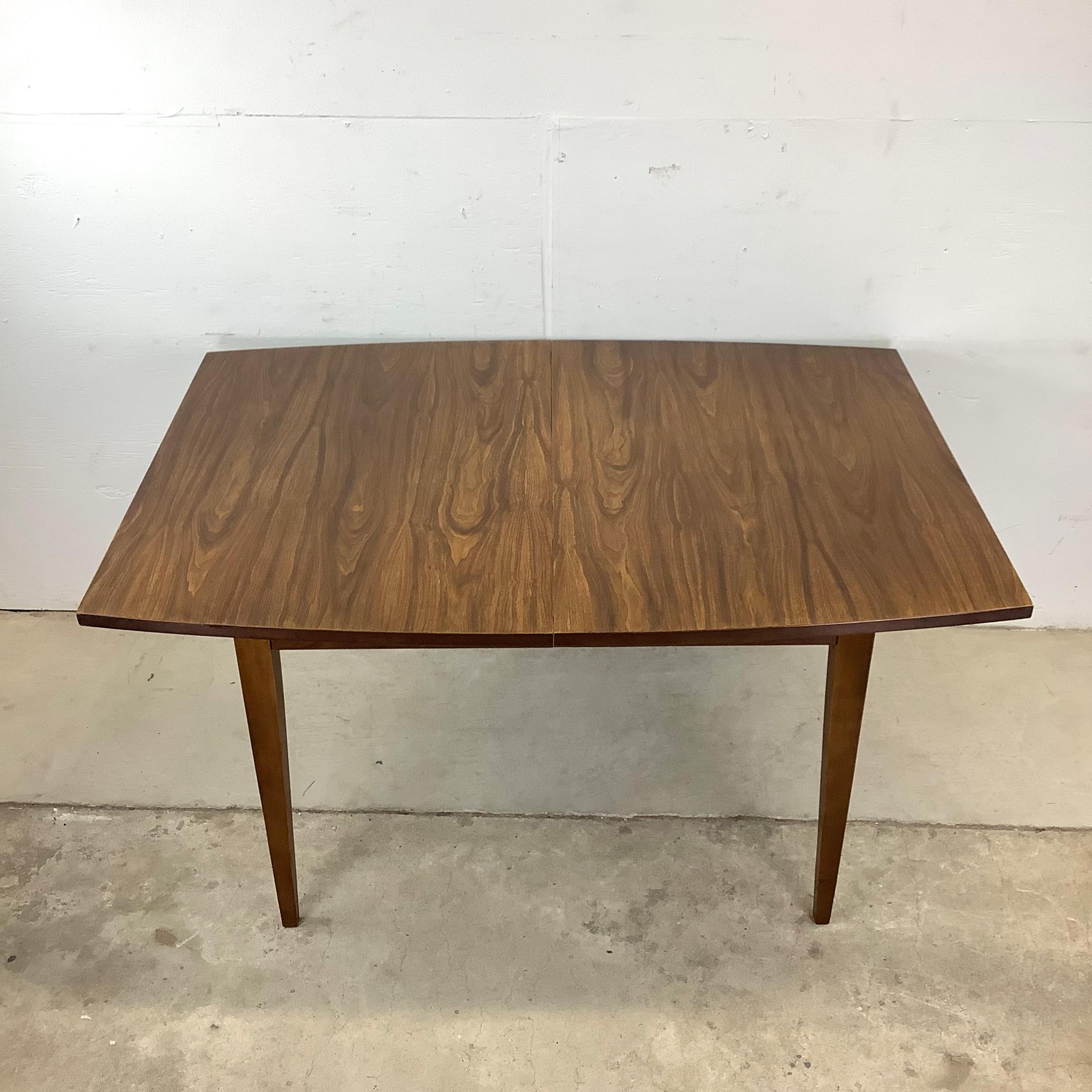 Cette table de salle à manger du milieu du siècle en finition noyer vintage est le mélange parfait d'une simplicité élégante et d'un design intemporel. La table est dotée d'un élégant plateau en faux bois qui imite le grain et la texture naturels du