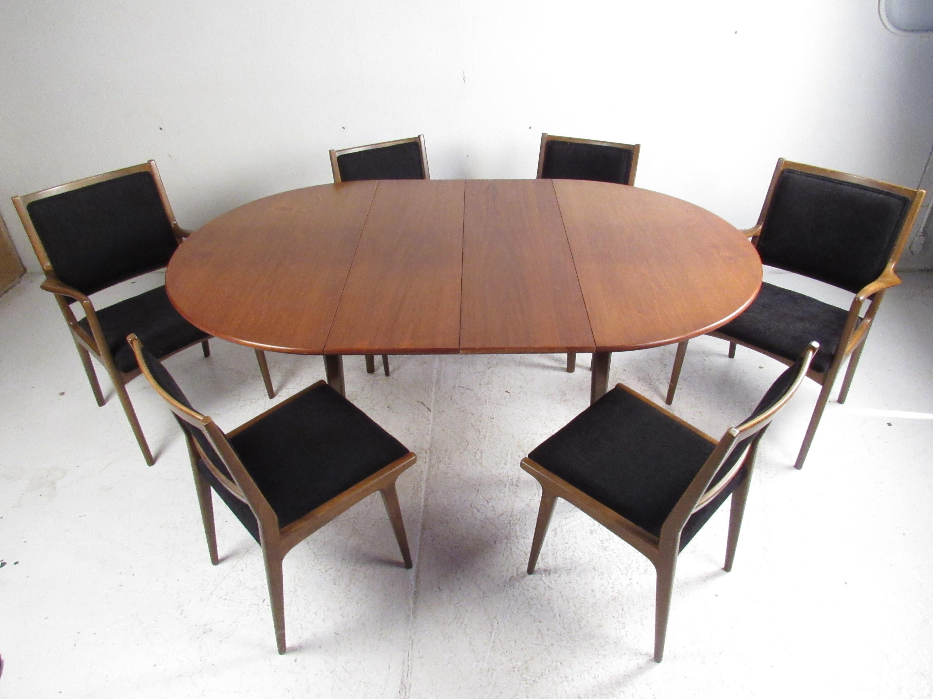 This stunning vintage modern dining set includes a dining table with two leaves, four dining chairs, and two arm chairs. An impressive design that boasts a round tabletop, long tapered legs, and stretchers for added sturdiness. The stylish set of