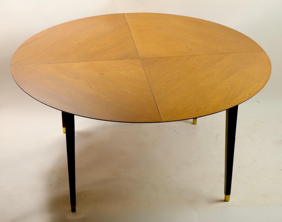 Architectural midcentury dining table having a round top with quartered line delineations and a beveled edge, on squared tapered legs with brass sabot feet Well constructed, nice usable scale, quality materials and sophisticated design. Clean, ready