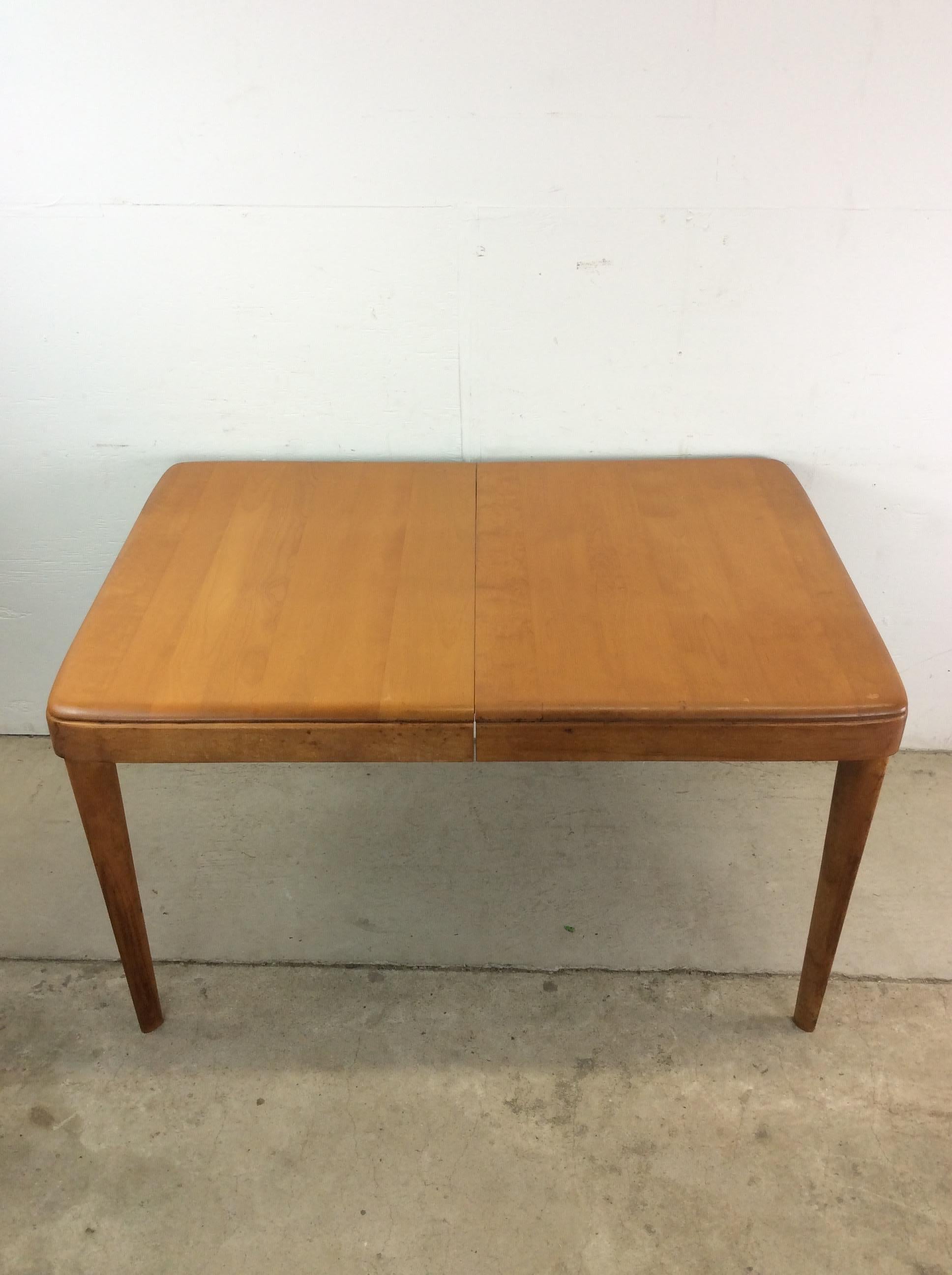 This mid century modern dining table by Heywood Wakefield features hardwood construction, original champagne finish, four removable legs, and a leaf for additional room. 
One 14” Leaf 
 Matching Heywood Wakefield dining chairs and servers available