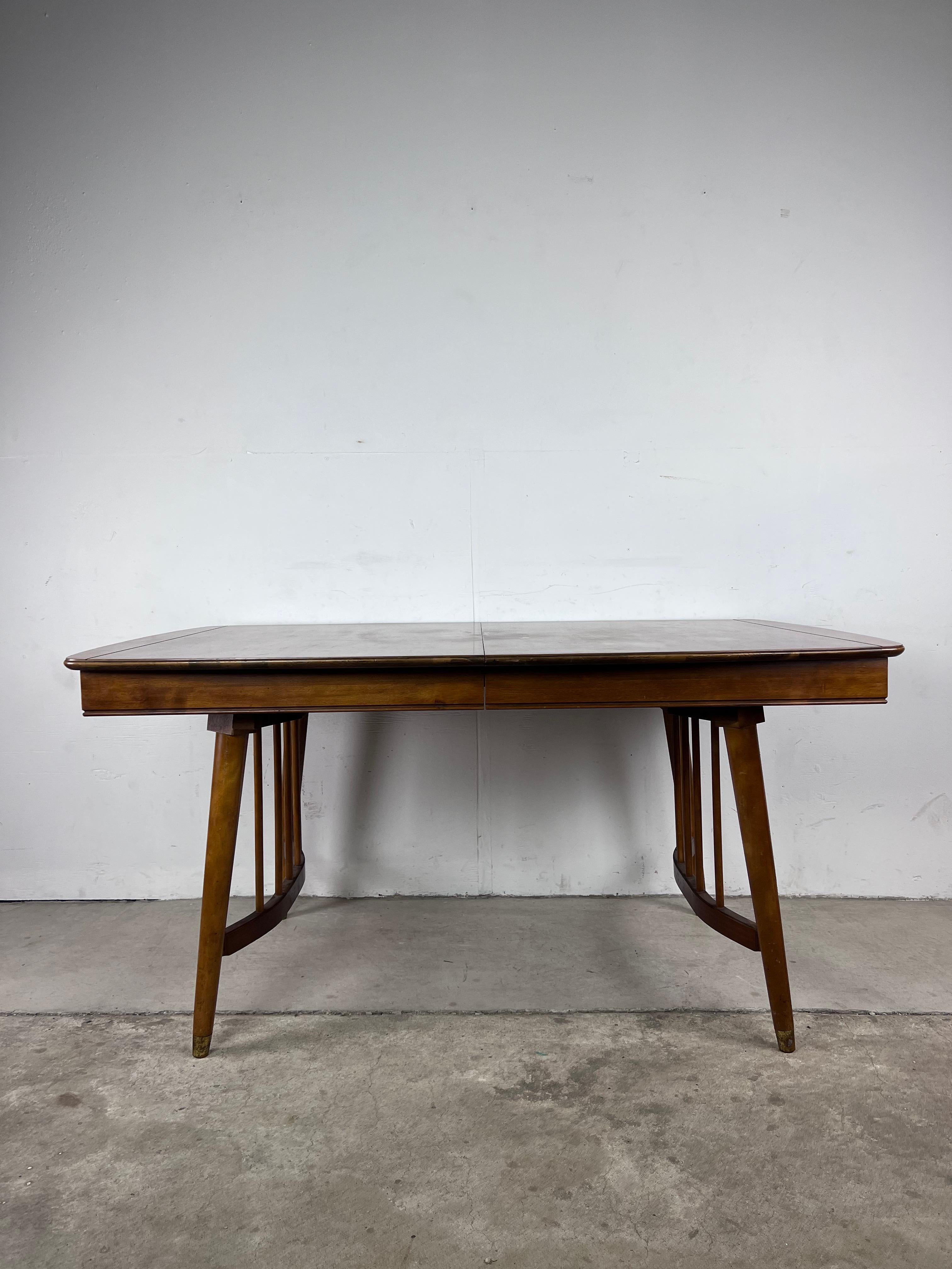 This mid century modern dining table by Ebert Furniture of Red Lion, PA features hardwood construction, walnut veneer with original finish, unique bentwood legs with brass capped feet, and a single 12