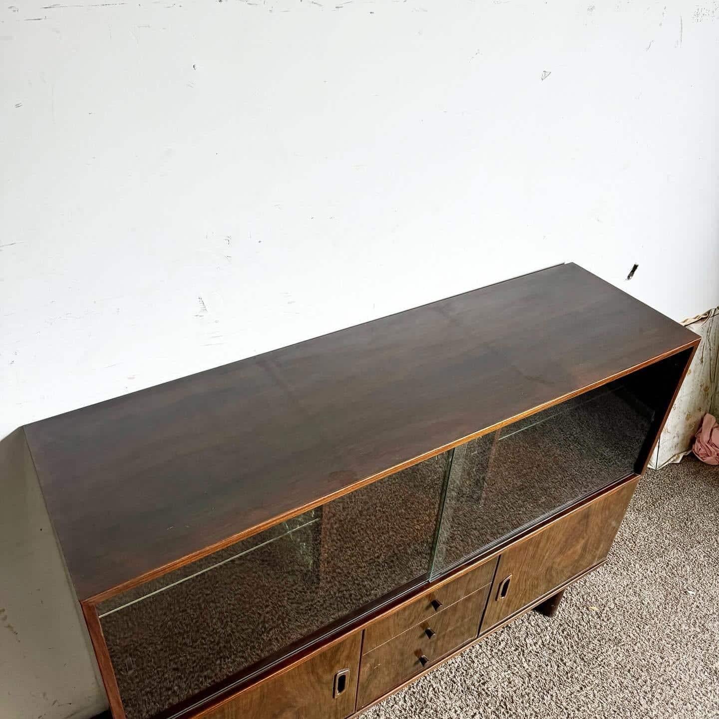 This stylish Mid Century Modern Display Cabinet combines form and function with clean lines and versatile storage. Featuring a glass-fronted upper section with adjustable shelves and a lower section with side cabinets and drawers, it adds