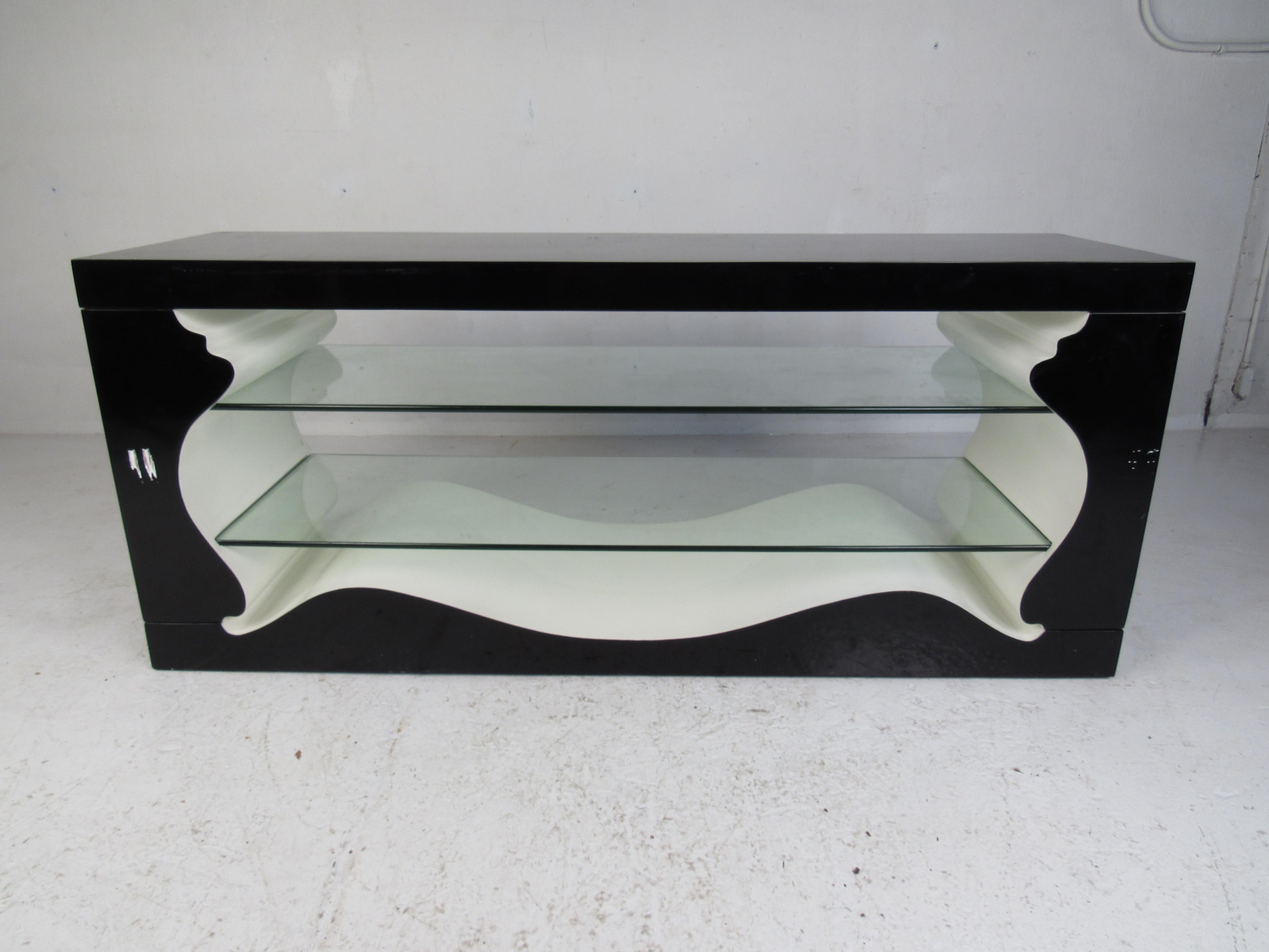 This beautiful vintage modern console features a sculpted design with two large glass shelves inside for displaying items. A unique shape with a black exterior and a white interior making this piece stand out. A versatile table that works perfectly