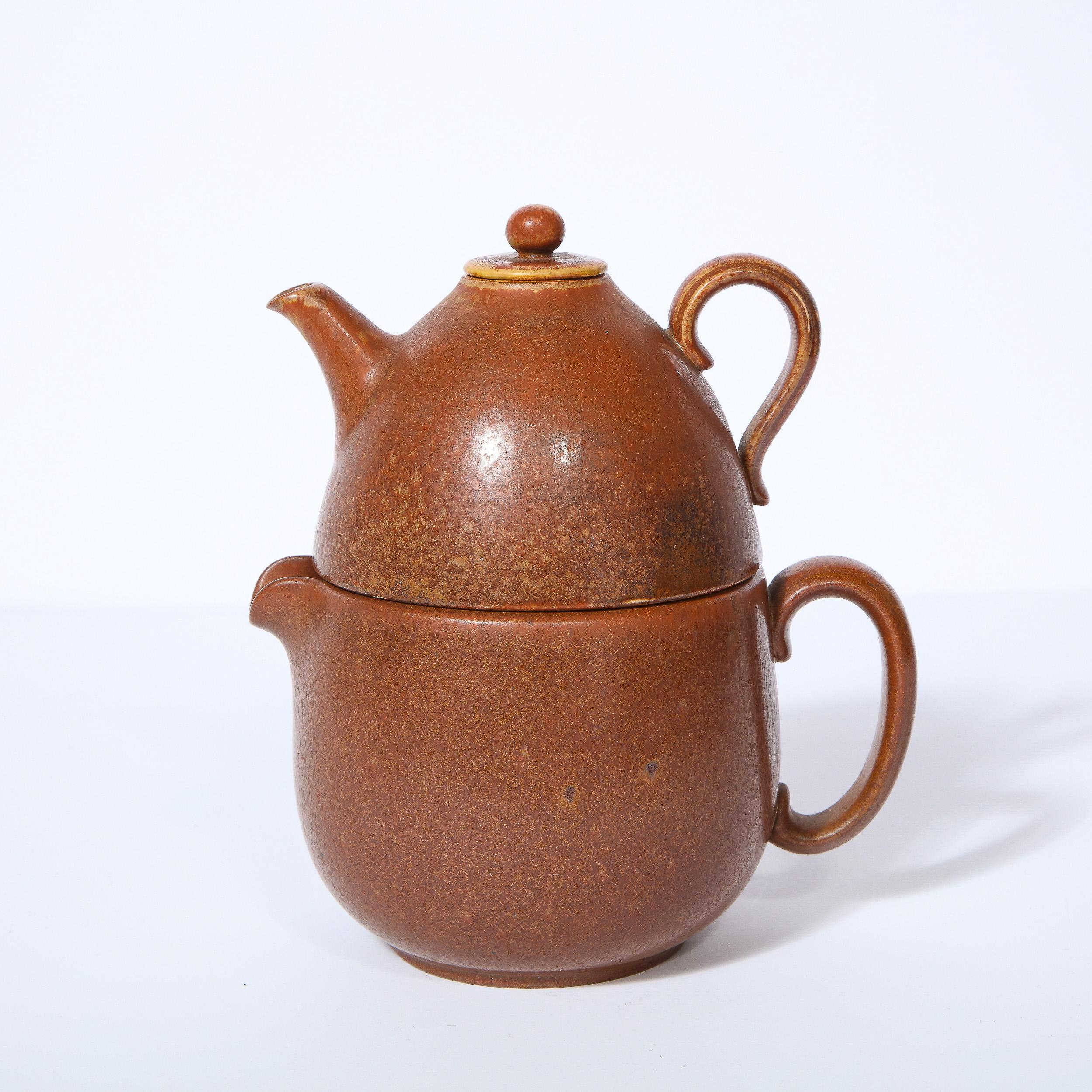 This refined Mid-Century Modern Scandinavian double teapot was realized by the esteemed Gunnar Nylund for Rorstrand in Sweden circa 1960. It features an ceramic stoneware teapot with a spout and curved handle onto which another domed teapot with a
