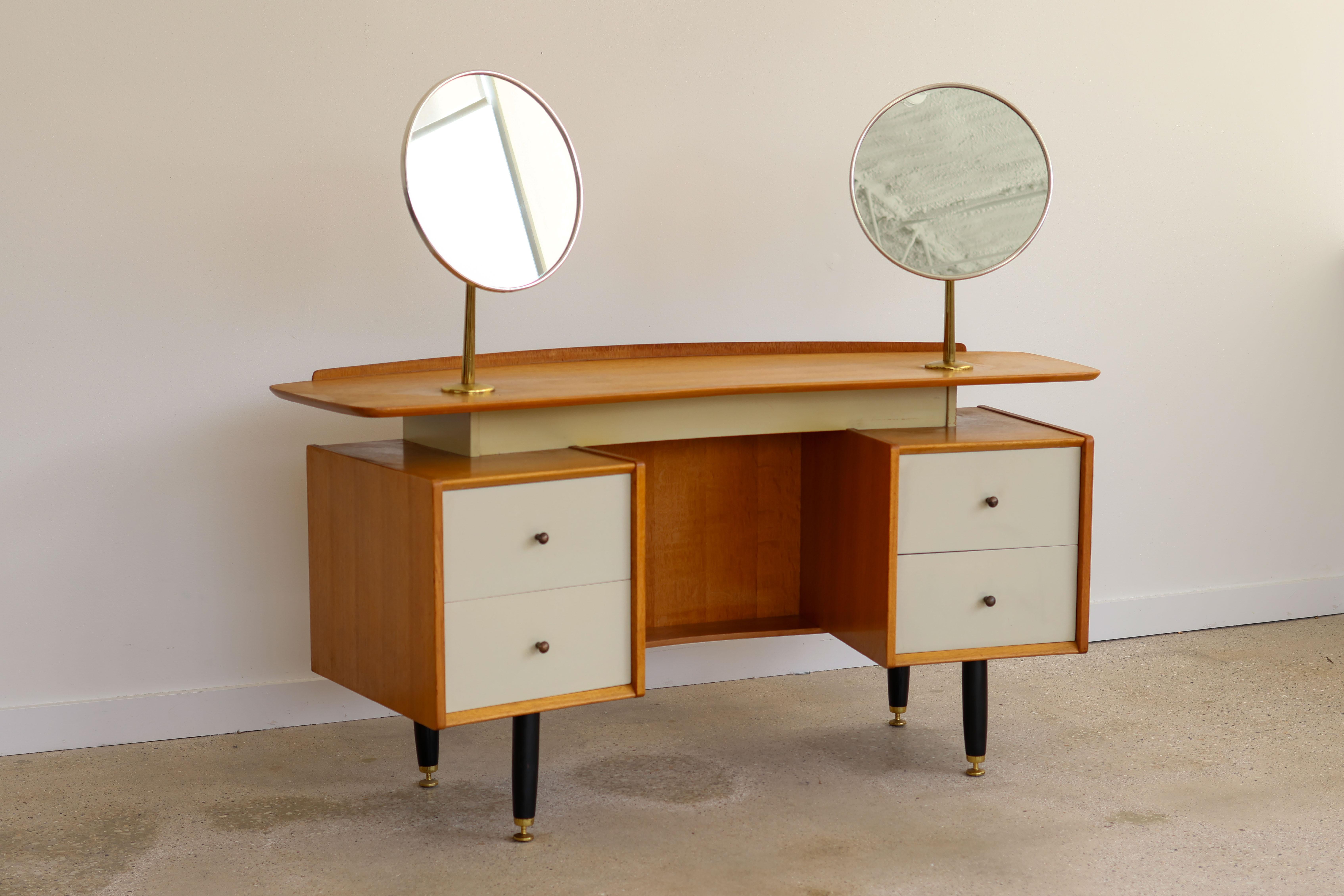 Mid Century Modern double mirror boomerang oak vanity.
Designed by E. Gomme for G-Plan.
Just imported from England.
Contrasting white lacquered drawers and ebonized wood legs.
Floating top.
Two fully swiveling mirrors on slender brass poles - giving