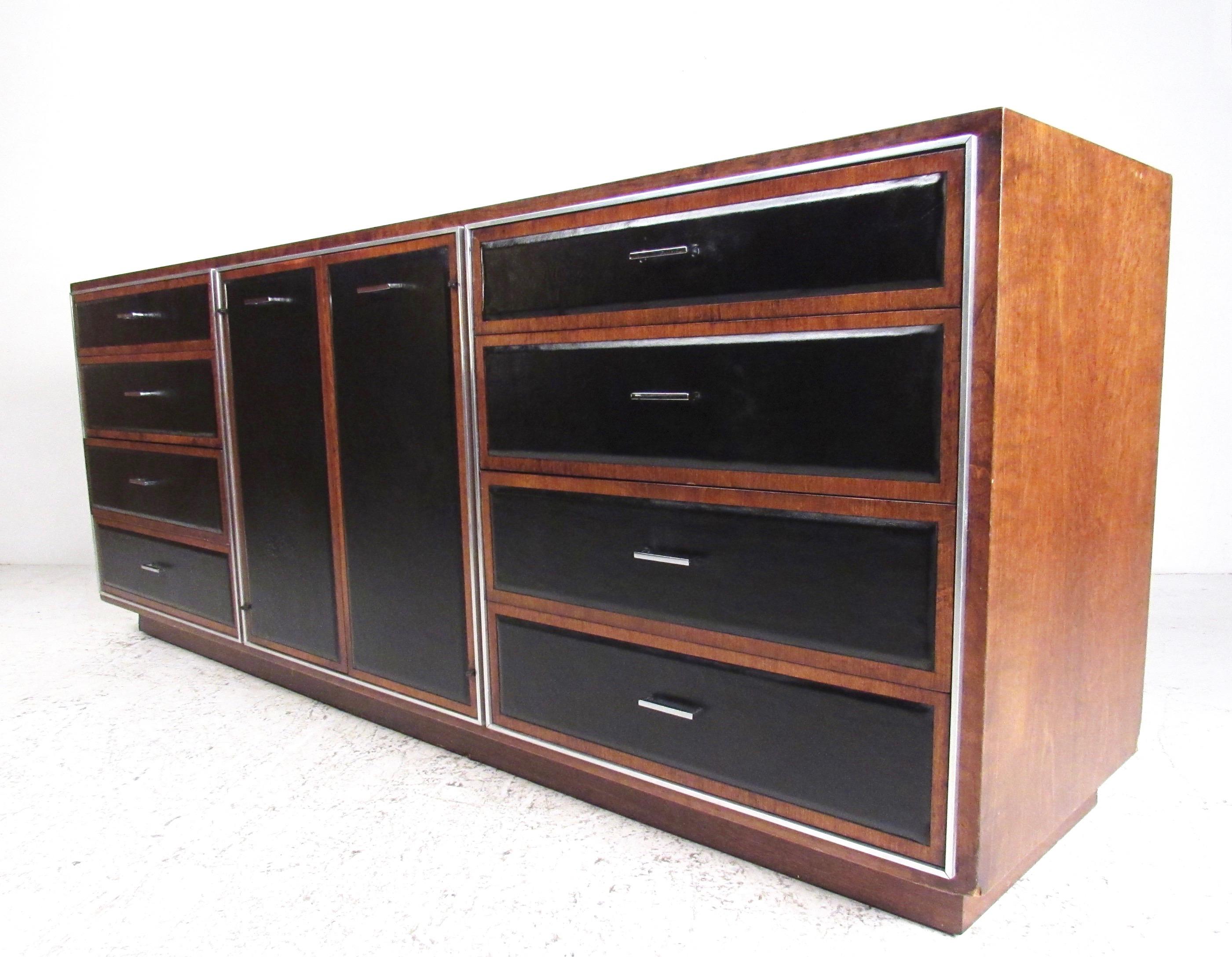 This stylish two-tone vintage bedroom dresser features rich wood finish mixed with black leatherette door fronts. Accented by chrome handles and offering nine spacious drawers for storage this long low Mid-Century Modern dresser makes a substantial