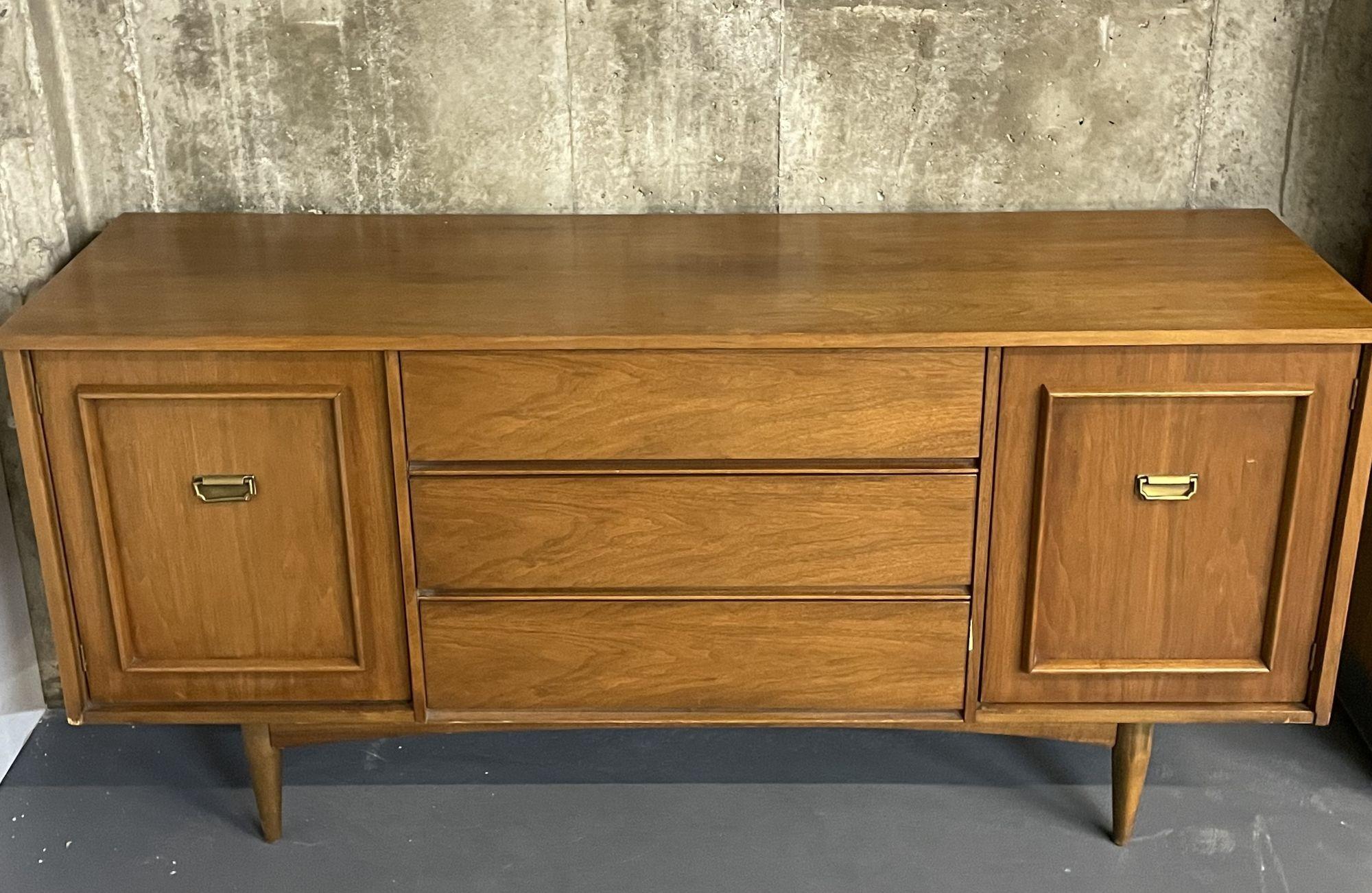 Mid-Century Modern dresser, chest or sideboard, walnut
 
A Mid-Century Modern dresser having three center drawers flanked by two doors concealing hidden drawers. Each door having Campaign chest style handles in brass. The case on tapering legs