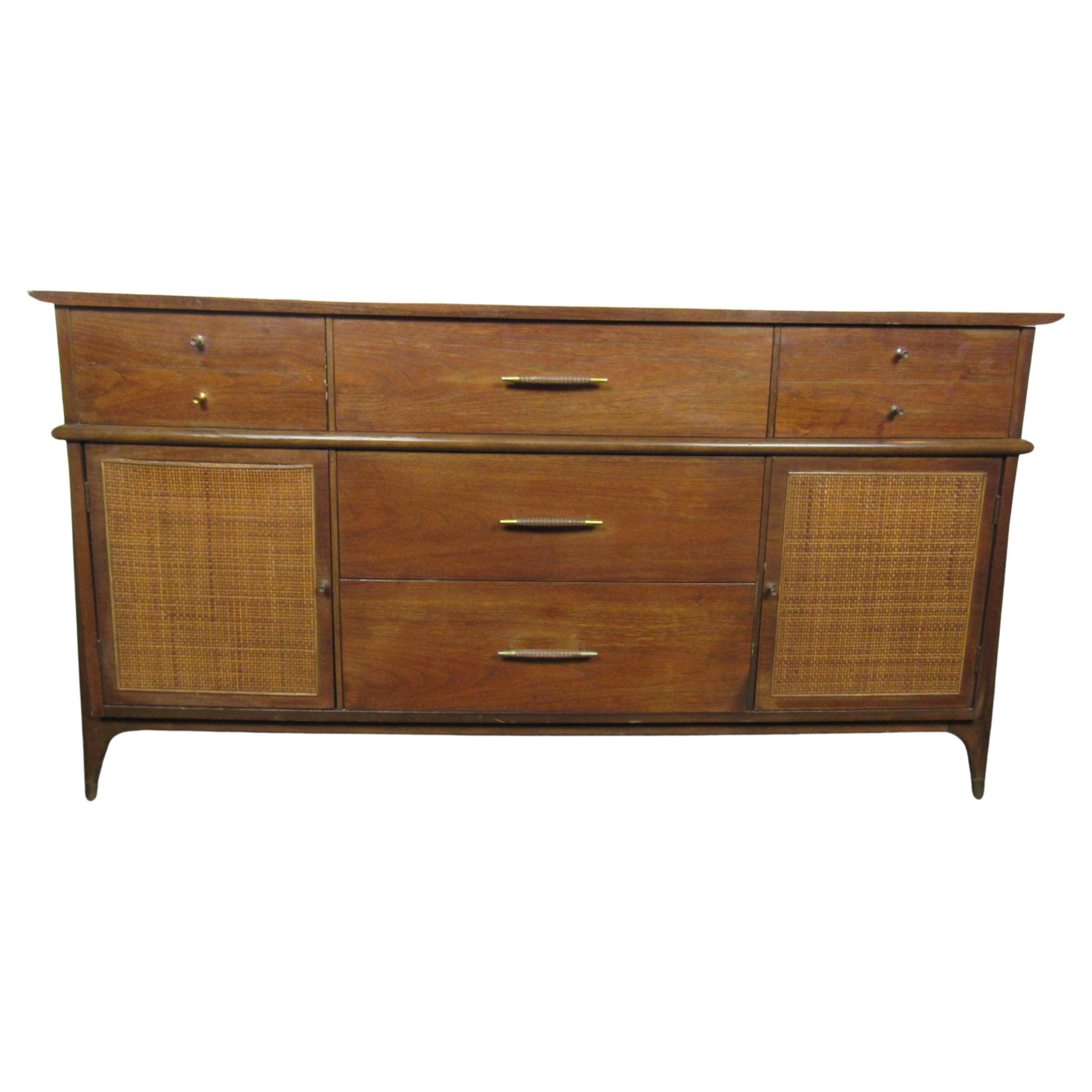 This Mid-Century Modern style dresser combines woven panels with walnut woodgrain and metal drawer pulls. Storage compartments and multiple drawers offer organization in a stylish design. Please confirm item location with seller (NY/NJ).