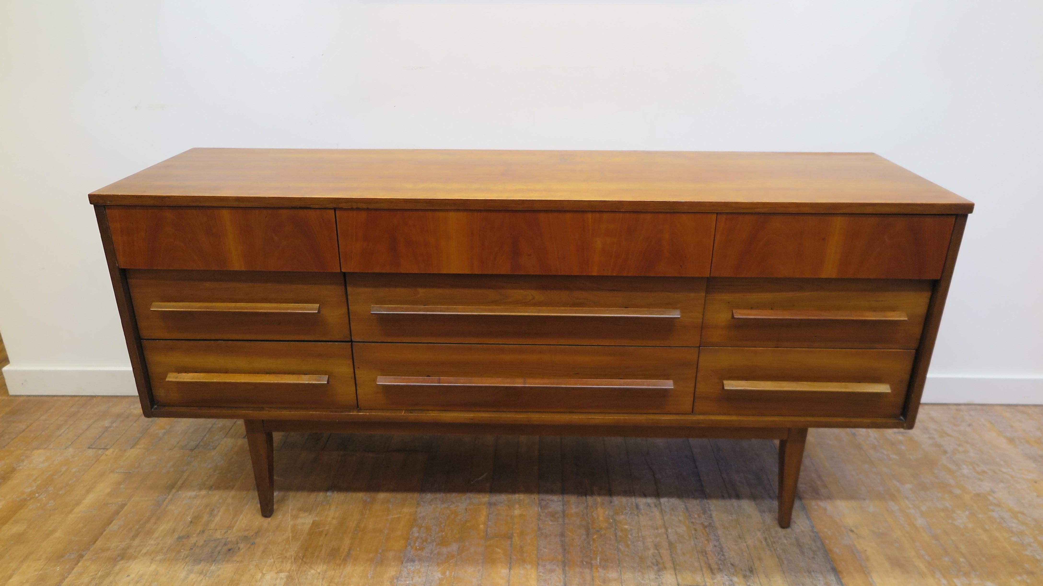 American Mid-Century Modern Credenza dresser by The Berkeley Co. Designers and Manufactures. Mid Century Modern dresser in Cherry wood with nine drawers on raised legs set on apron. Great design elements top drawers protruding out with cut out