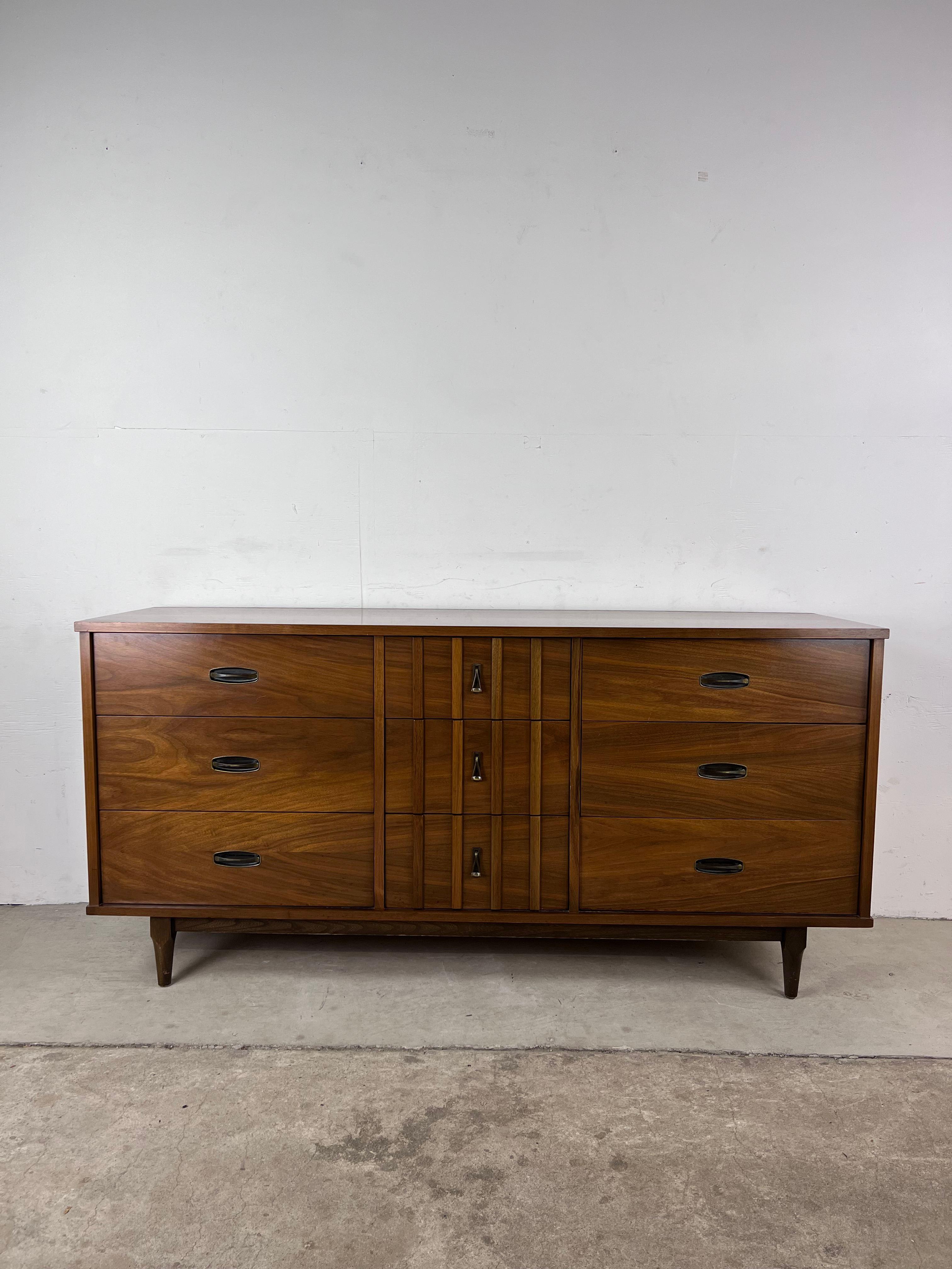 This mid-Century Modern lowboy dresser by Krug furniture features hardwood construction, walnut veneer with original finish, nine dovetailed drawers with brass hardware, and tapered legs.?? Matching nightstand and highboy dresser available