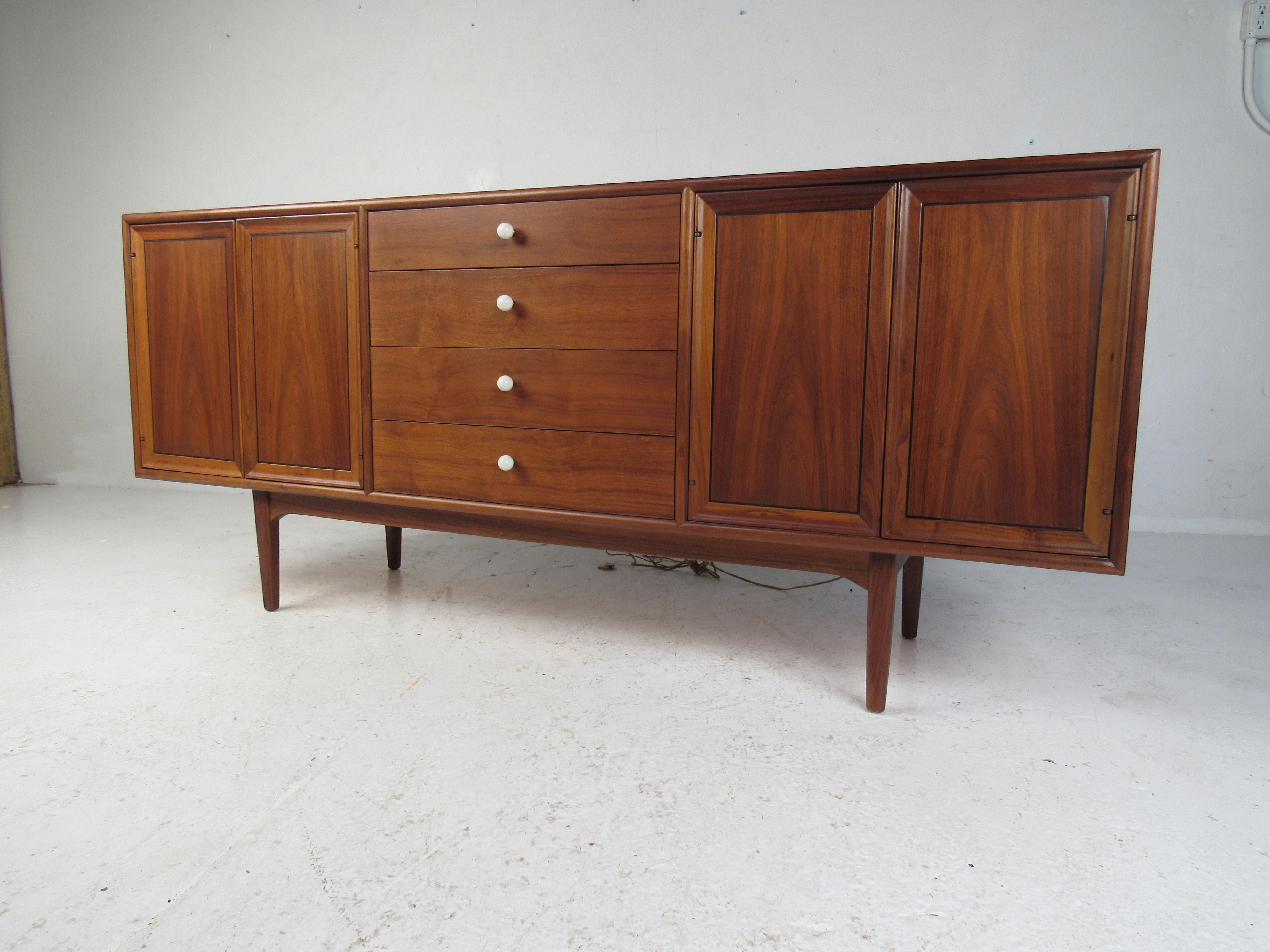 This stunning midcentury case piece by Drexel boasts unusual white drawer pulls and elegant walnut wood grain throughout. This gorgeous sideboard offers plenty of room for storage within its four hefty drawers and large compartments hidden by