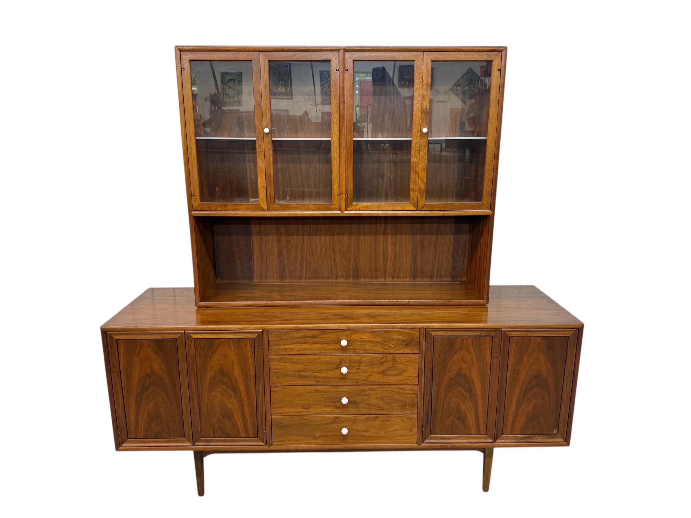 This listing is for a Mid-Century Modern Drexel Declaration Walnut 2-Piece China Cabinet. Featuring a straight line two piece design, display cabinet top with four glass doors that open up to milk glass shelves, sideboard base with push button doors