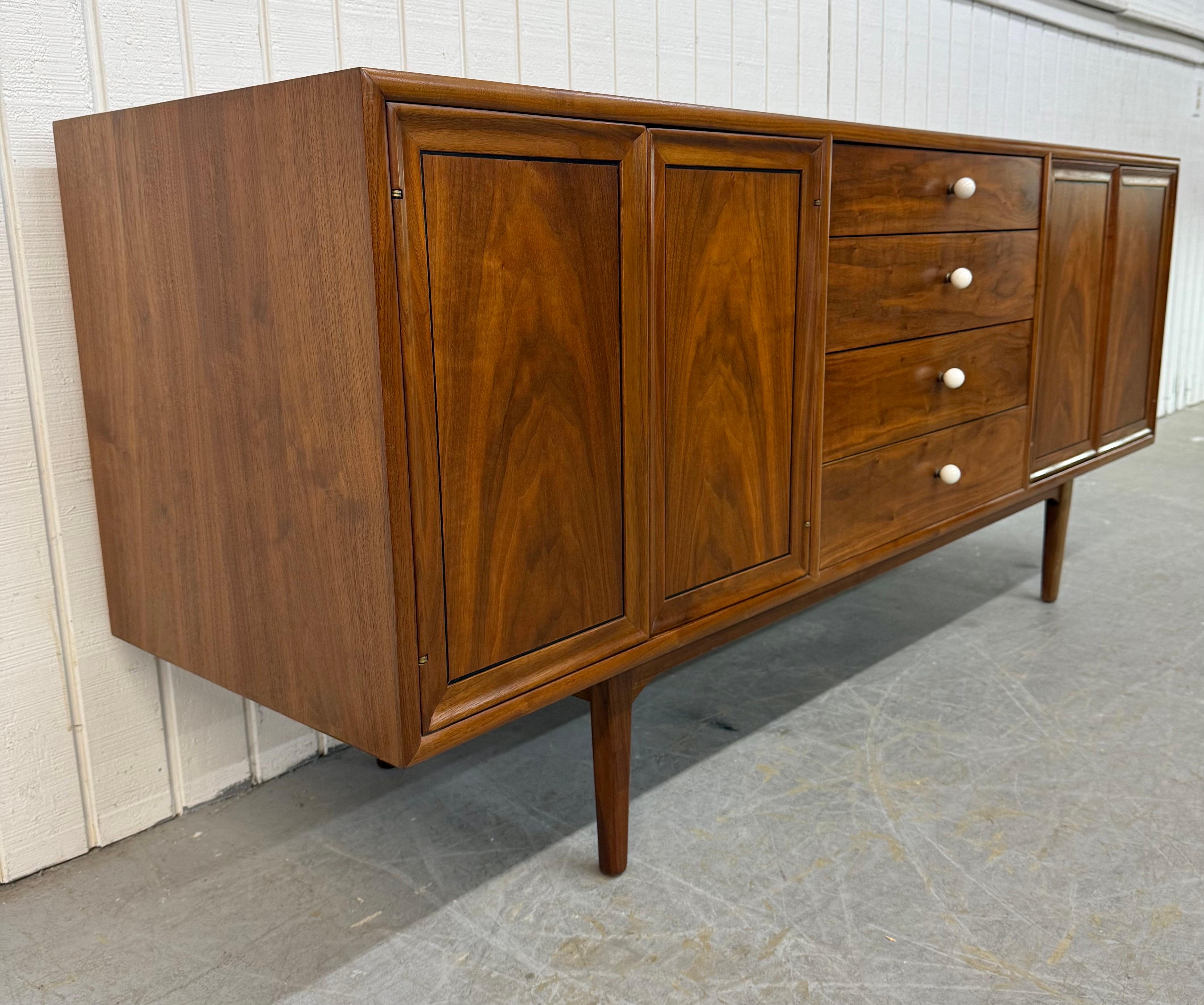 This listing is for a Mid-Century Modern Drexel Declaration Walnut Sideboard. Featuring a straight line design, push doors on each end that open up to storage space, four center drawers with round milk glass knobs, modern legs, and a beautiful