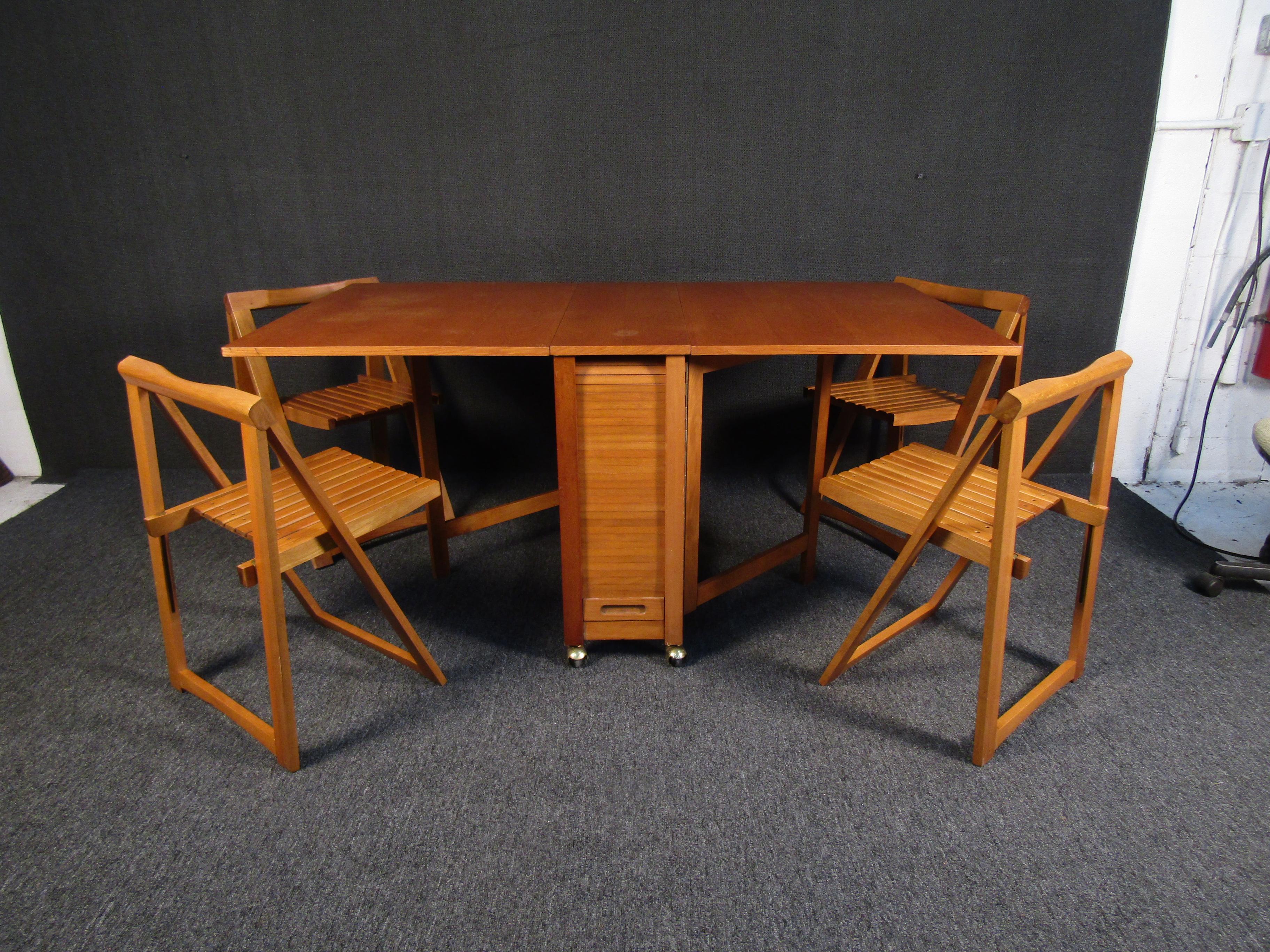 A gorgeous Mid-Century Modern style dining room set with a drop leaf table and four folding chairs. A compact folding design is complete with chairs that store away underneath the table. Rich wood grain makes this set an elegant addition to any