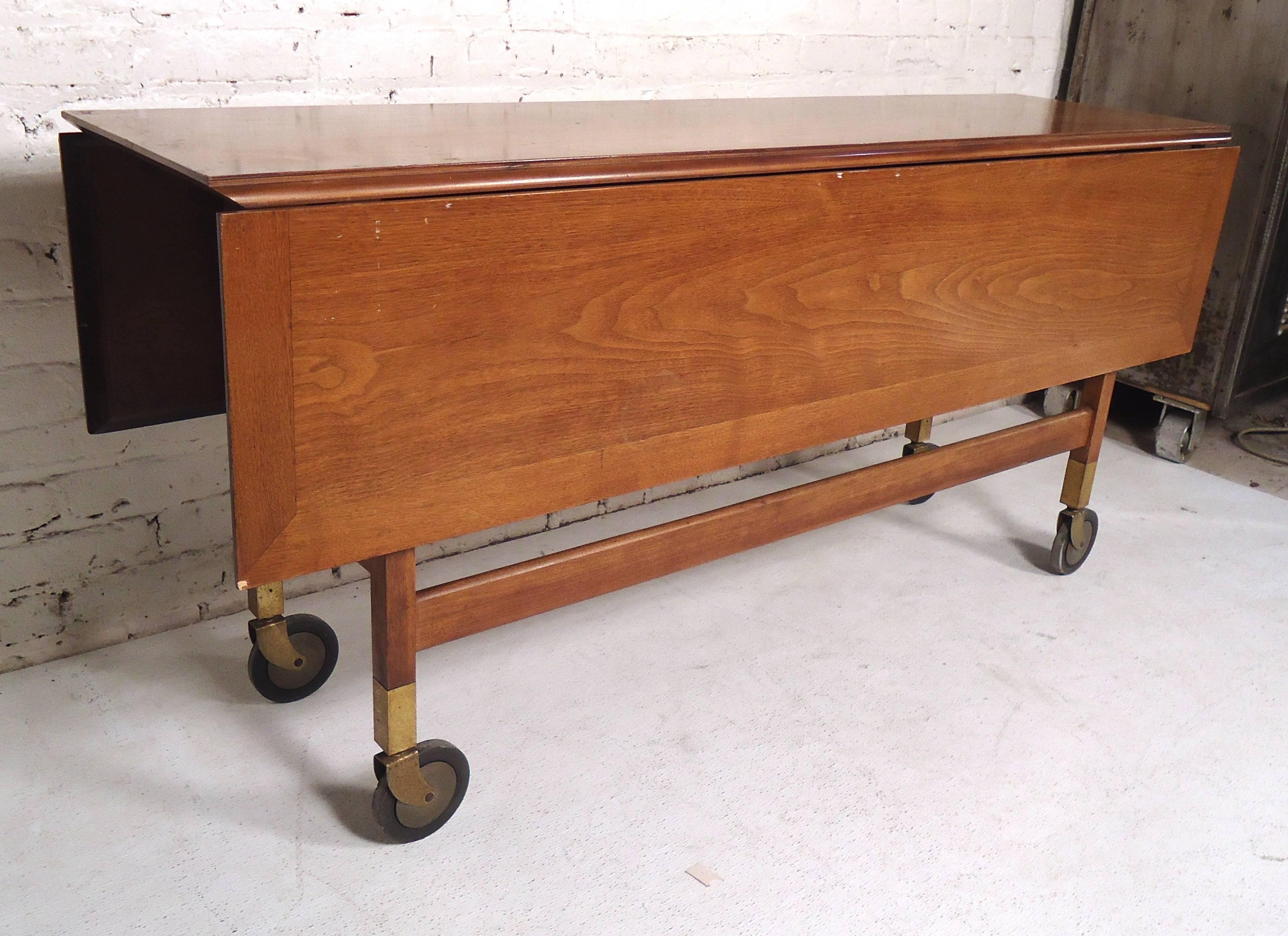 Large vintage-modern drop-leaf table featuring beautiful walnut grain, brass accents, on a set of four wheels.
Center is 15