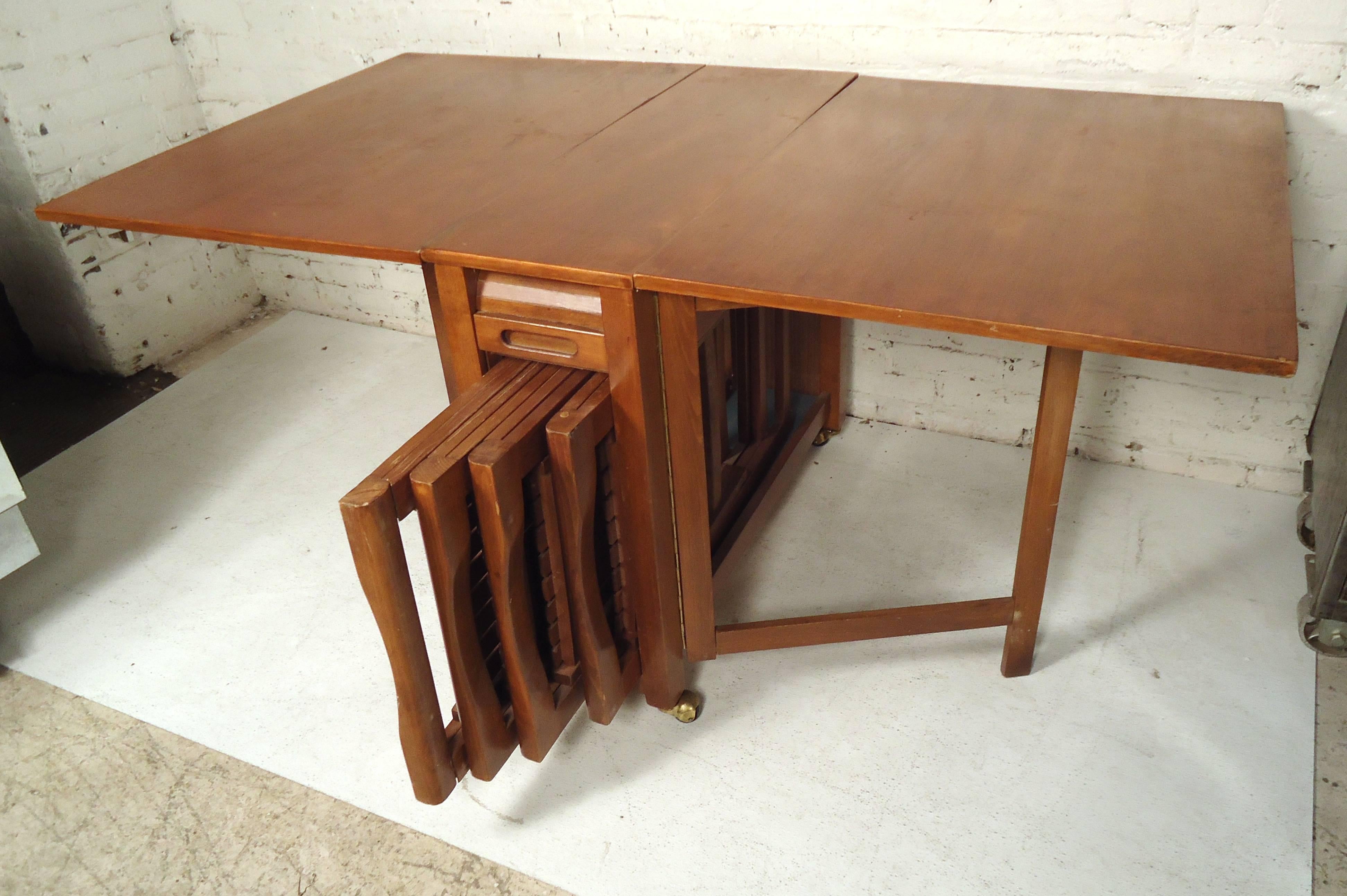 Impressive vintage modern compact design with four unique folding chairs and a drop-leaf dining table. Sleek design offers the ability to stow all four chairs within the table hidden behind a tambour door. Sturdy and stylish piece with gate legs and