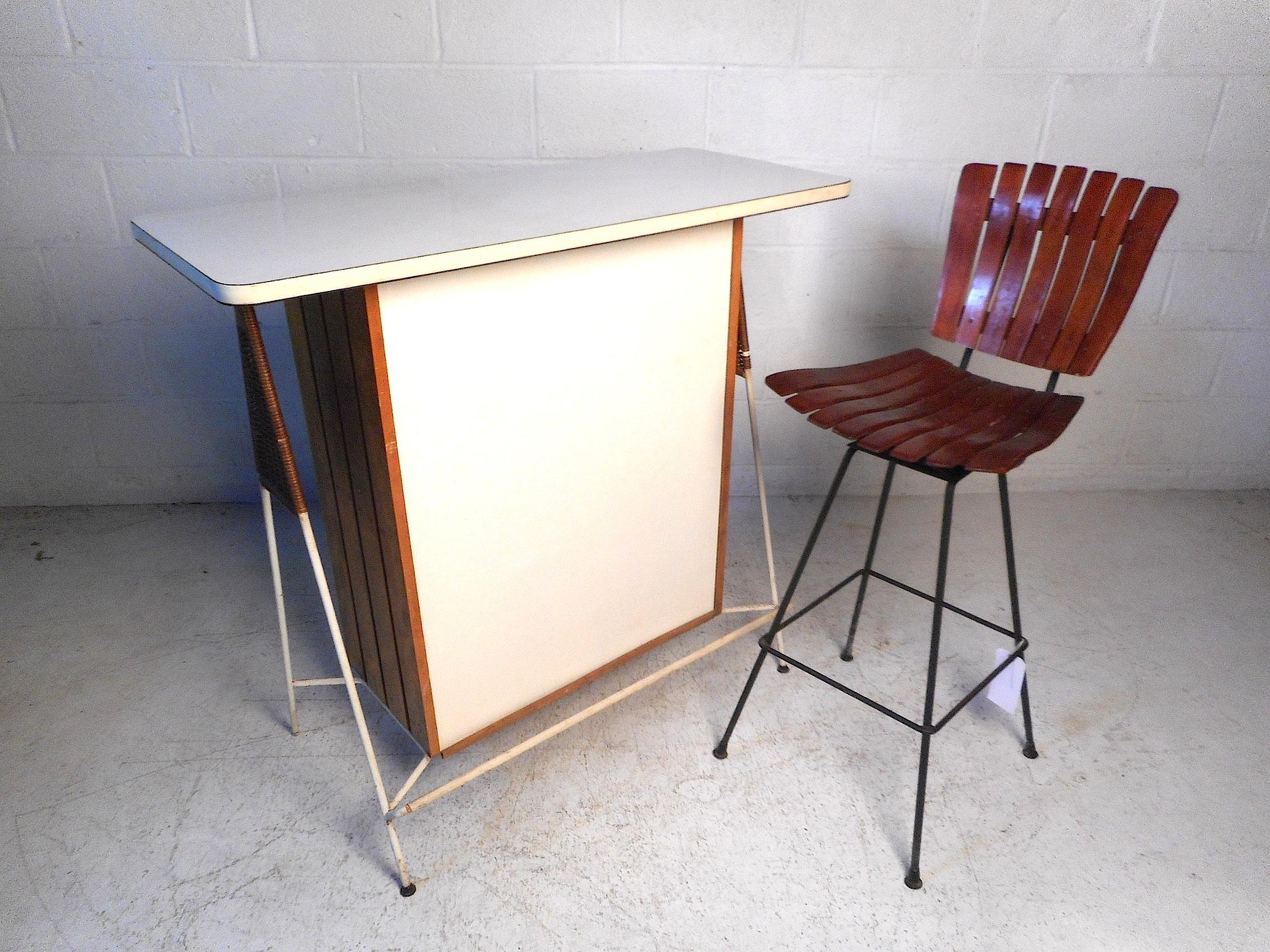 This stylish midcentury bar by Arthur Umanoff features a sleek metal frame, white laminate tabletop and front, and unusual wicker accents on the sides. Sure to impress in any home, office, or business' modern interior. Circa 1960's. Stool not