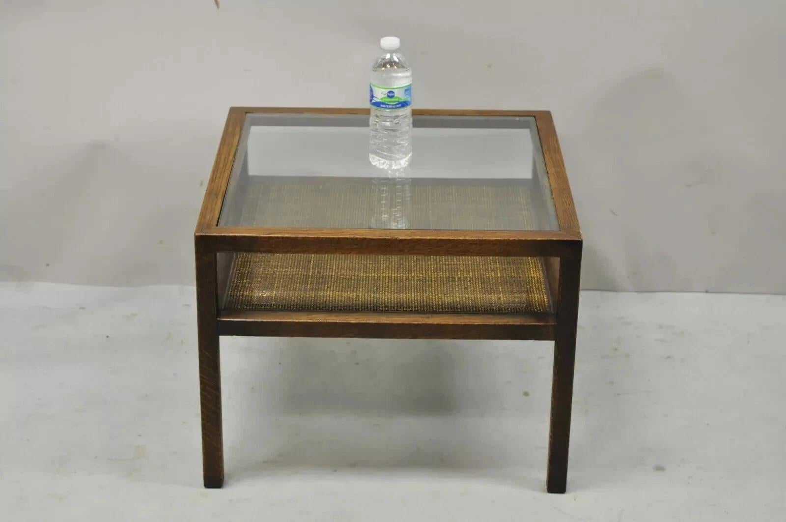 Vintage Mid Century Modern Dunbar Style Oak & Cane 2 Tier Glass Top Square Side Table. Ce meuble est doté d'un plateau en verre encastré, d'une étagère inférieure en rotin, d'un cadre en bois massif, d'un beau grain de bois et de lignes épurées et