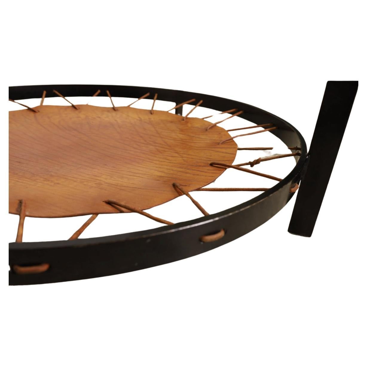 Mid century modern Round glass Safari sling leather coffee table on black lacquered metal base. Lower circular Magazine or Newspaper shelf in brown leather held up by rope. Table shows normal Use wear minor scratches on Round glass top. The leather