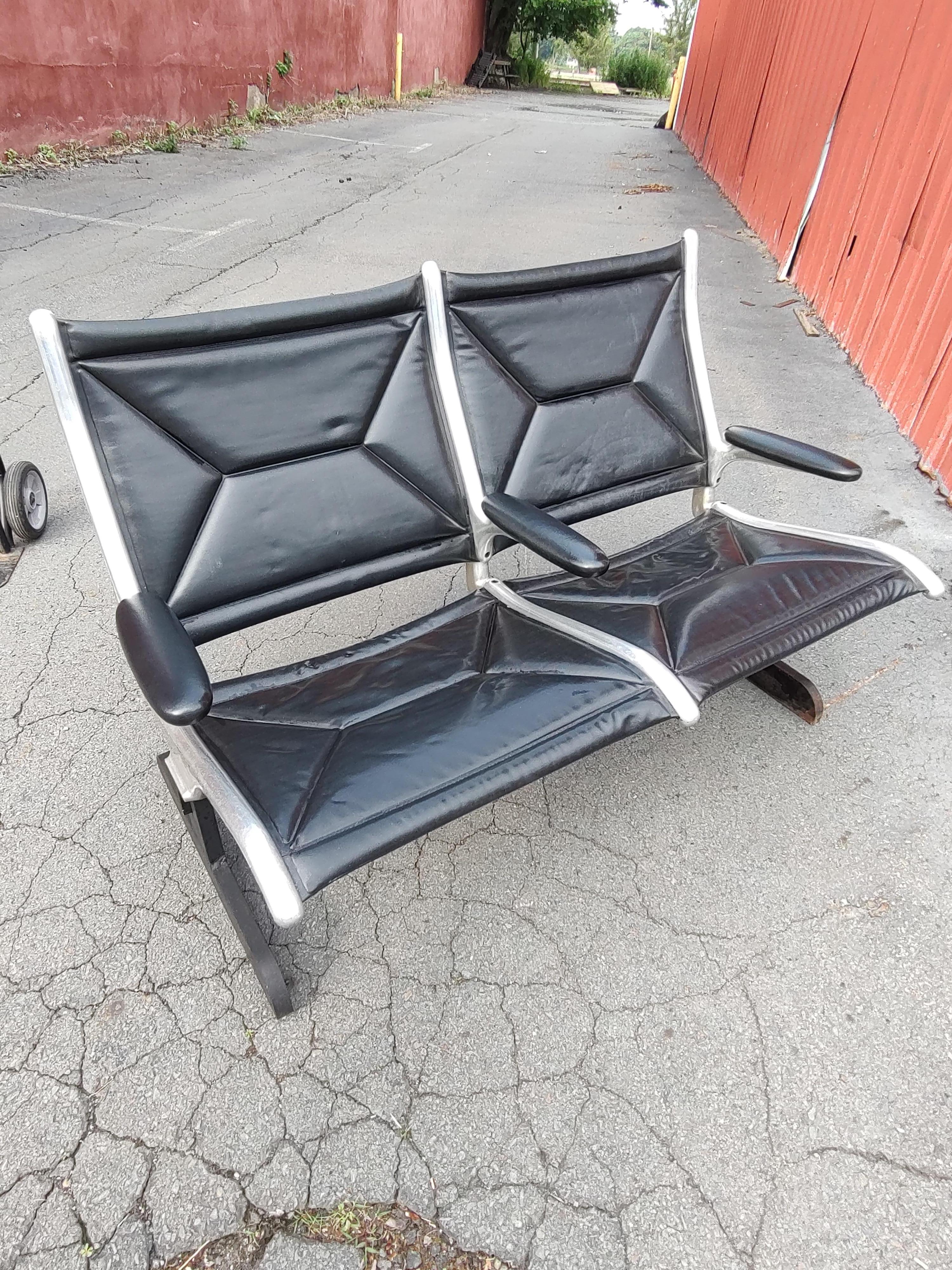 Fabulous two seat tandem airport seating designed by Charles Eames for Herman Miller c1960. Classic in design and still in service today. Die cast aluminum with steel I beams and base for stability and support. Cross stitched black leather in