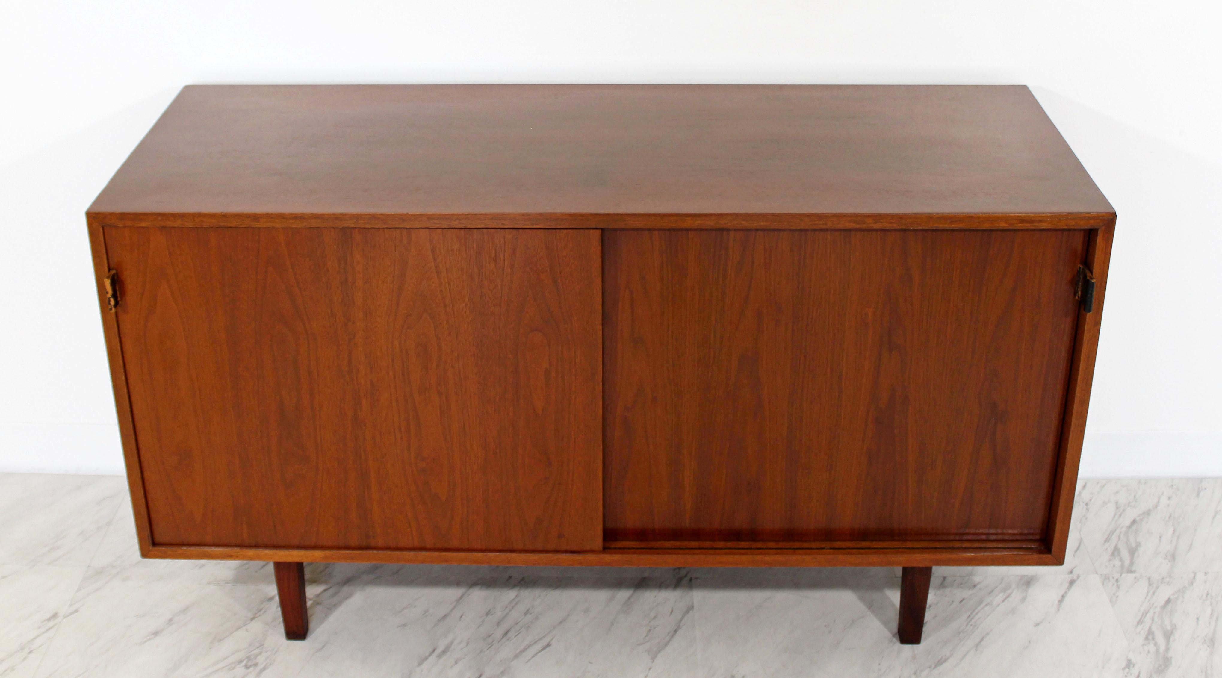 For your consideration is a captivating early version walnut credenza, with sliding doors that have leather pulls and three shelves, by Florence Knoll, circa the 1960s. In very good condition. The dimensions are 48