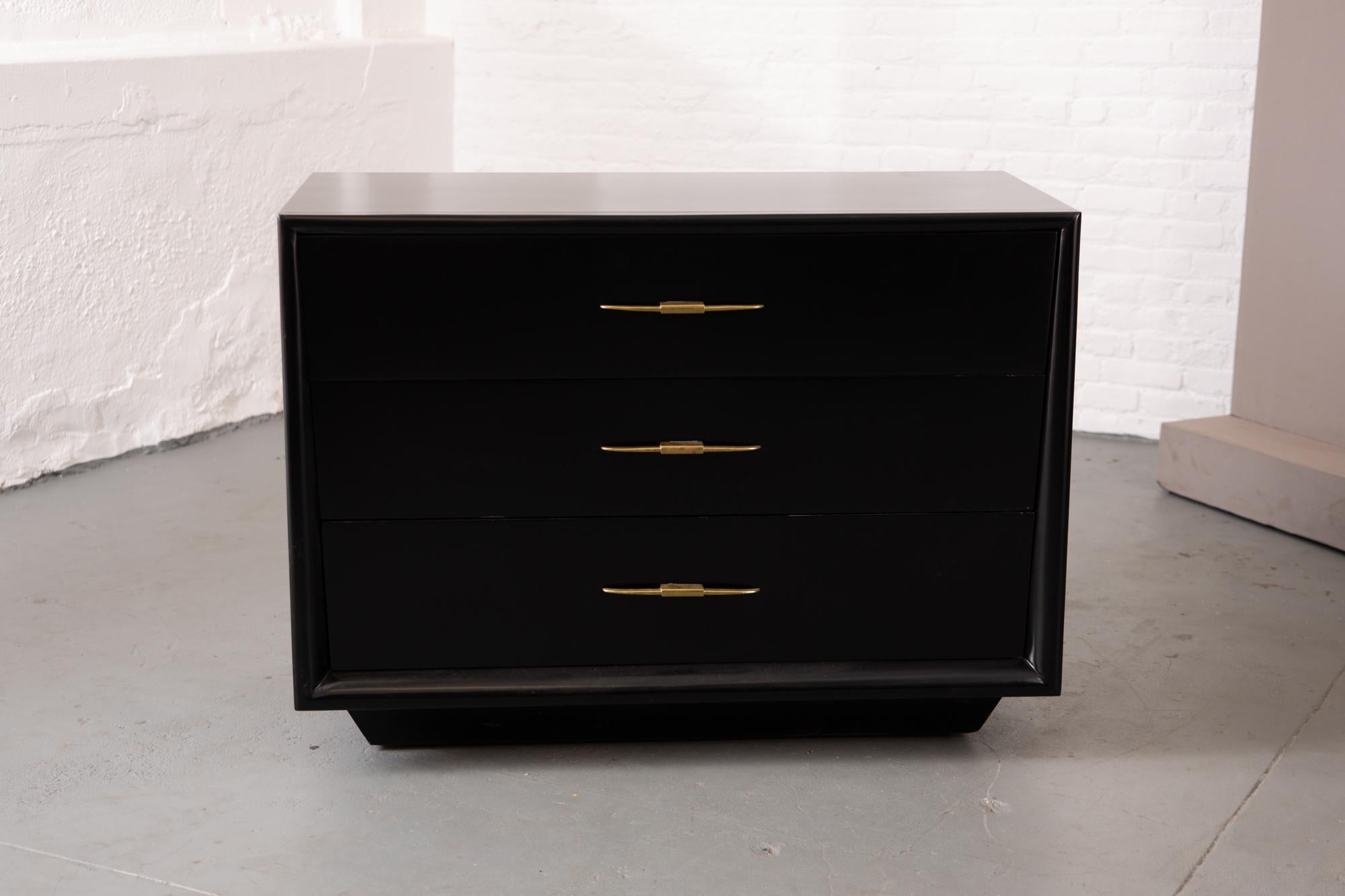 Handsome MCM American three drawer ebonized chest with patinated brass pulls. Recently refinished. Tapered face detail. Sits atop a rectangular base with hidden small casters.