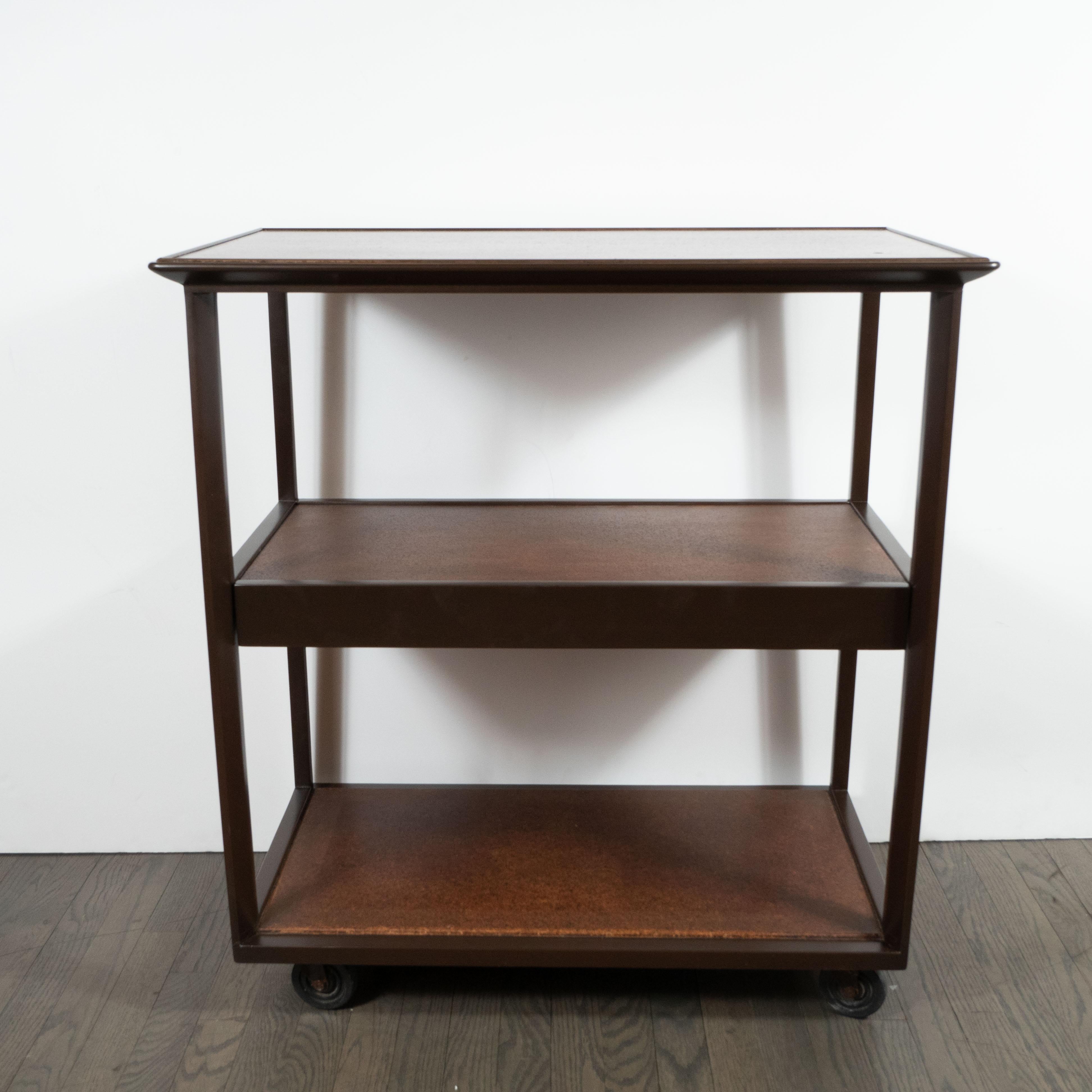 This refined bar cart was designed by the illustrious American firm Dunbar, and handmade in Berne, Indiana, circa 1960. It features three rectangular tiers in with tawny brown centers and ebonized walnut perimeters. There is a drawer that pulls out