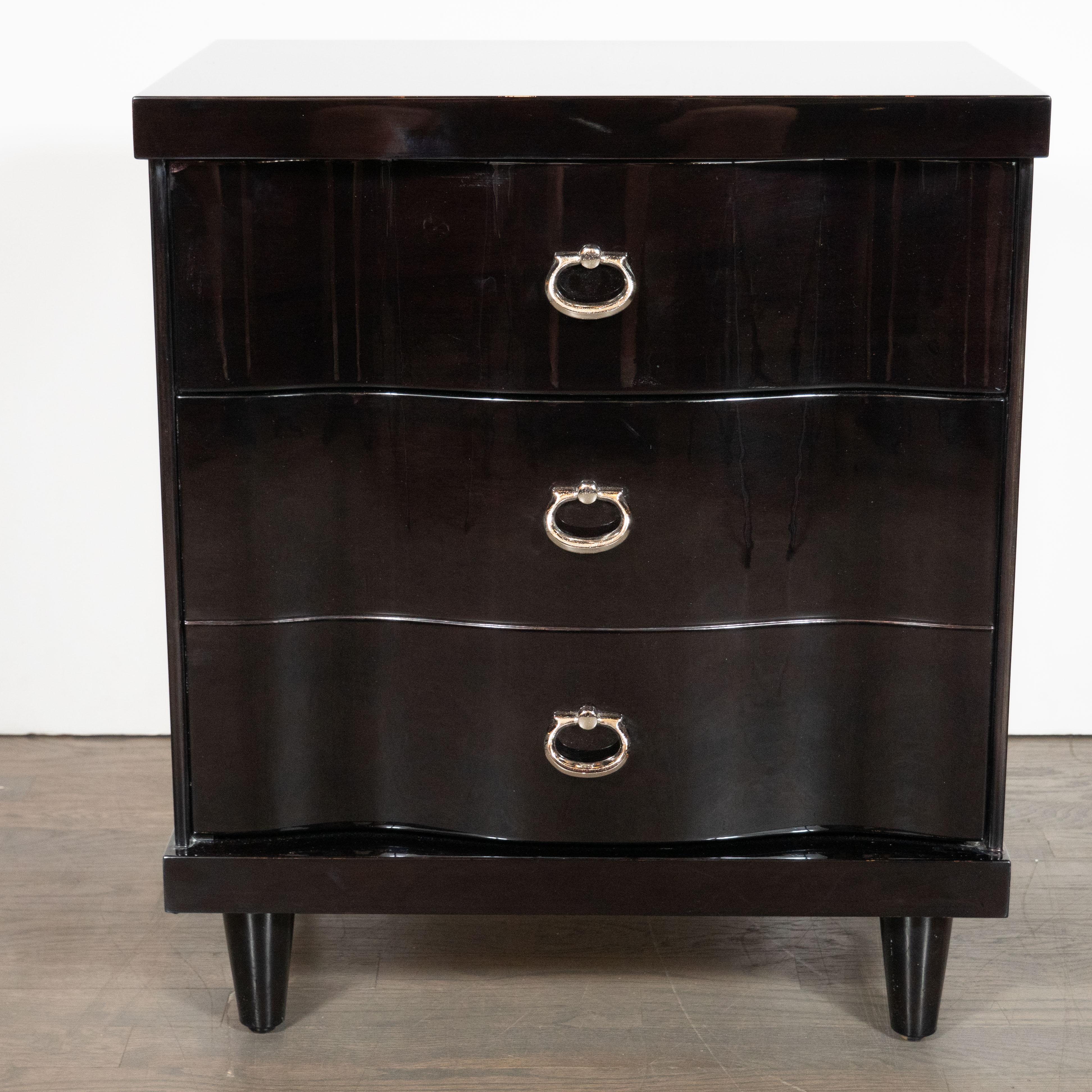 This pair of Mid-Century Modern nightstands was designed in the United States, circa 1950. The nightstands each have a minimal ebonized walnut frame supported by four tapered legs. Inset within each frame are three, stacked undulating bowfront